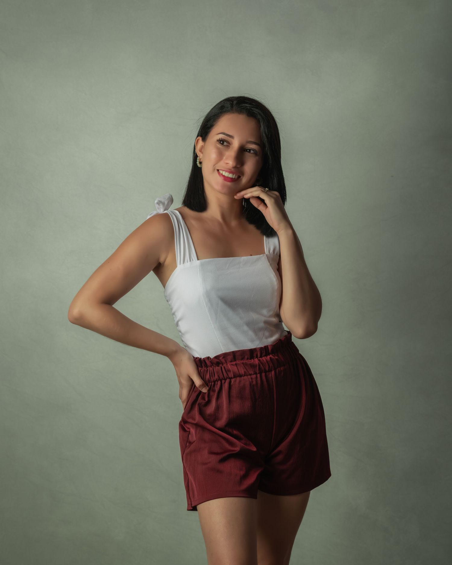 Portrait of a woman in white top and burgundy shorts posing against a gray background.
