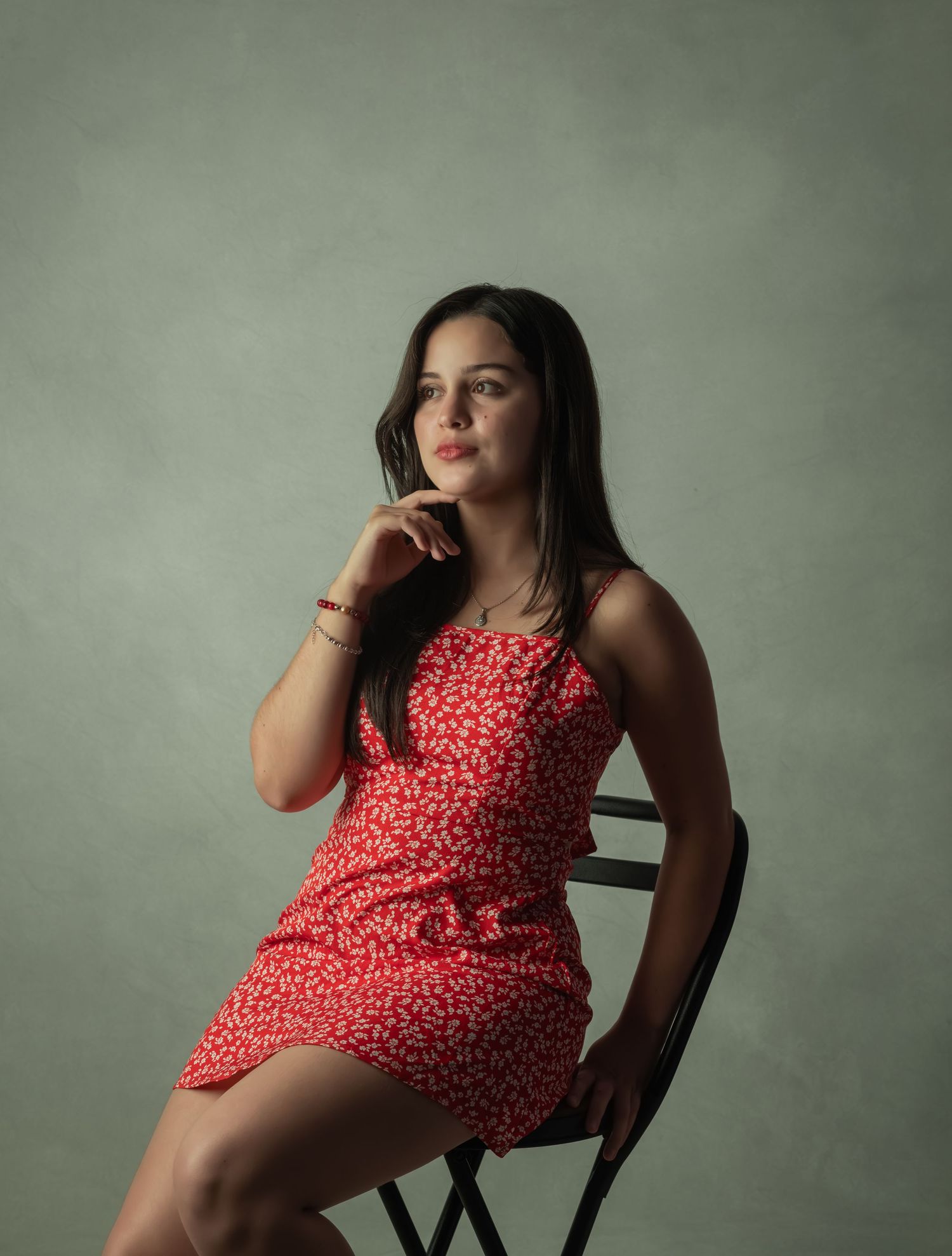 Portrait of a woman in red floral dress sitting elegantly on a chair.