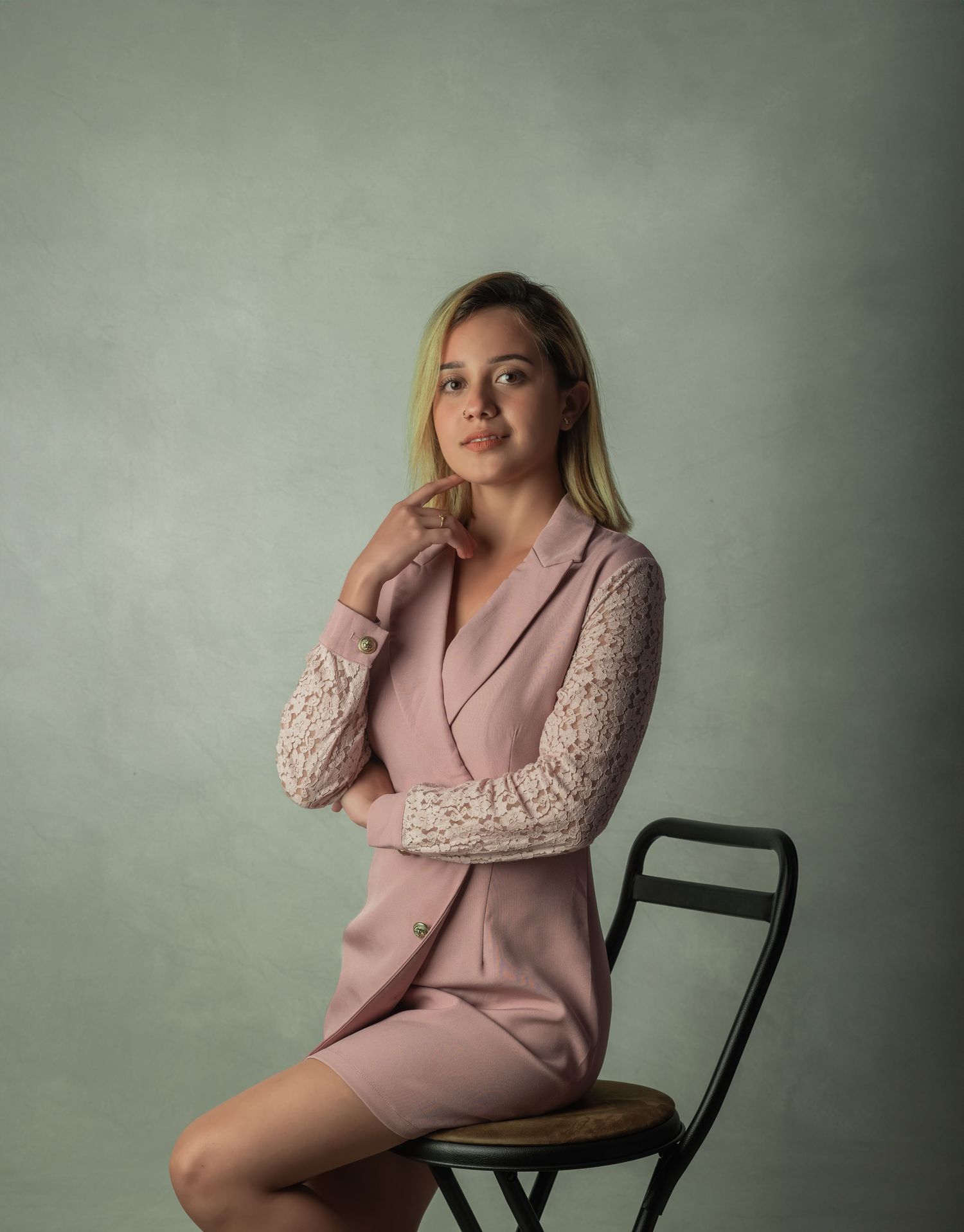 Professional portrait of someone wearing a pink blazer with lace sleeves seated on a chair.