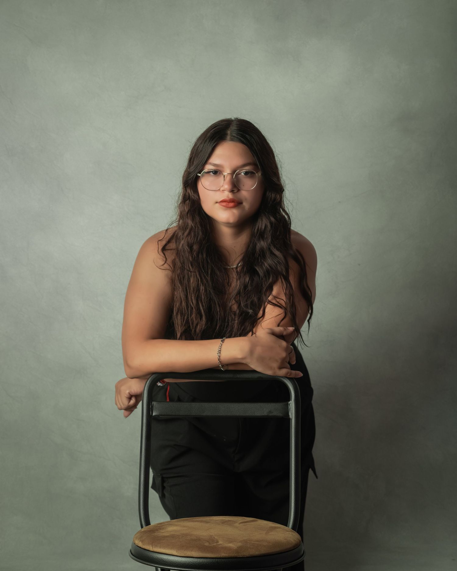 Studio portrait with artistic lighting showing a seated figure in casual attire against a grey background.