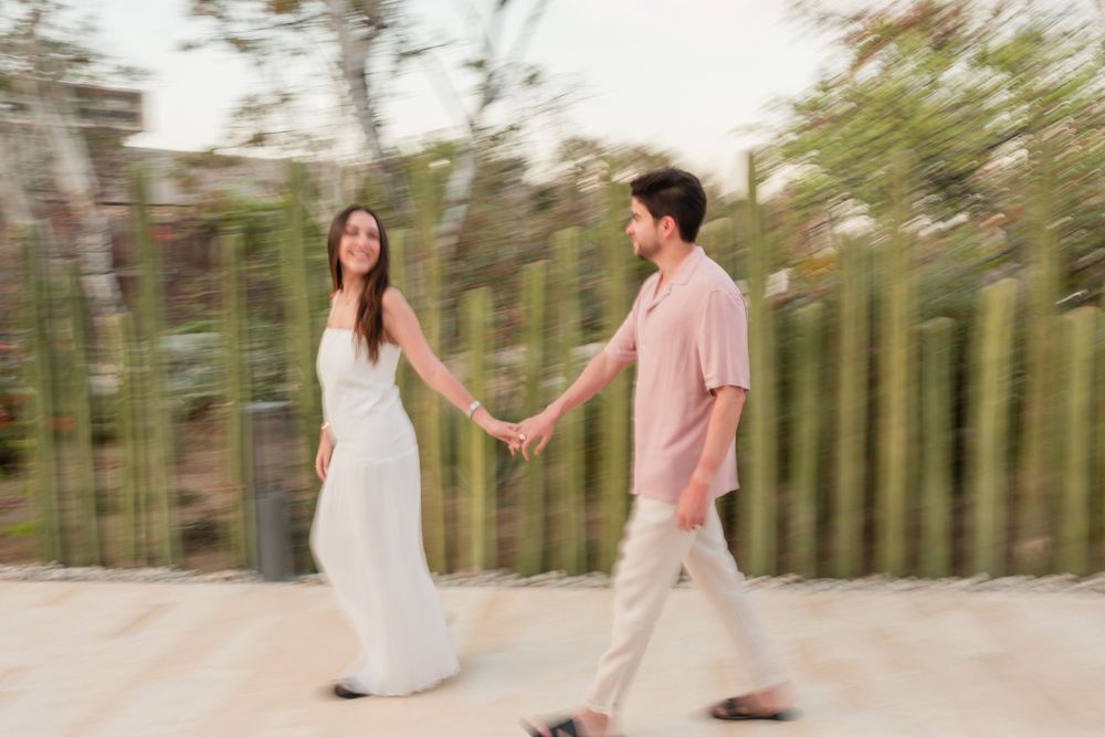 A couple in coordinated outfits walking hand in hand along a path with bamboo trees in the background.