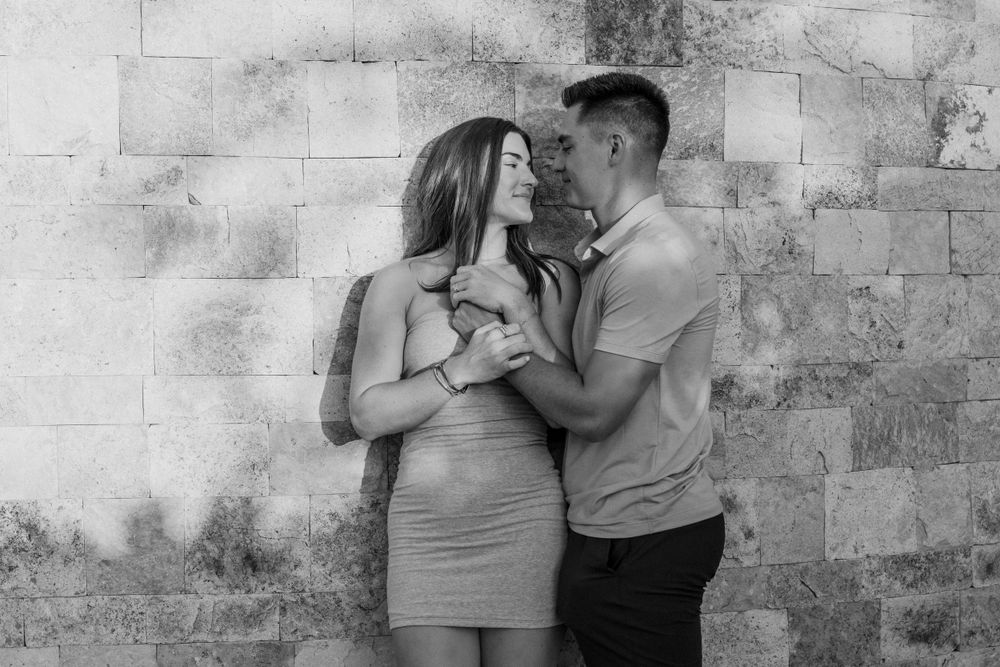 Romantic couple poses against stone wall in black and white portrait.