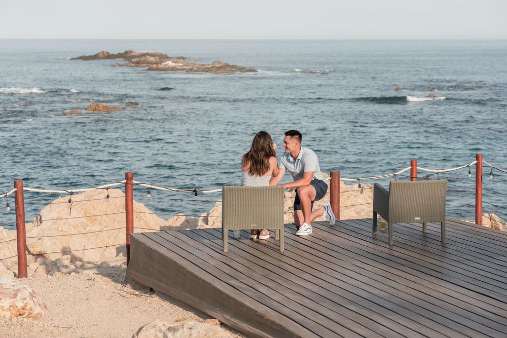 A couple sits together on a seaside deck overlooking the ocean.