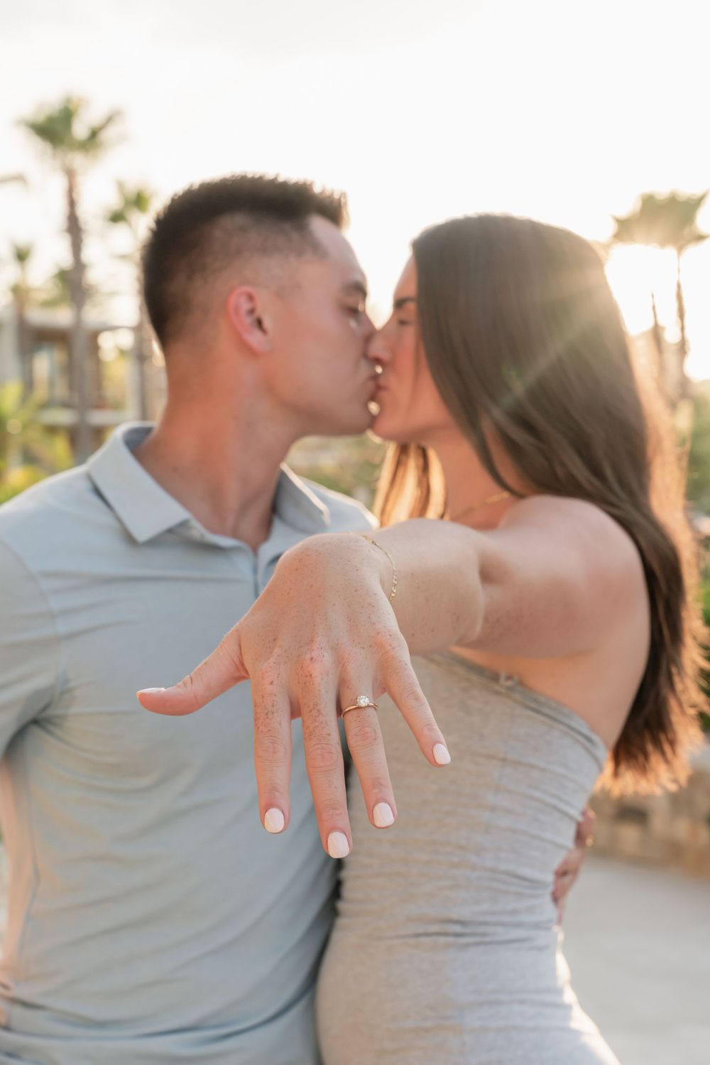 Newly engaged couple sharing a kiss with engagement ring in focus.