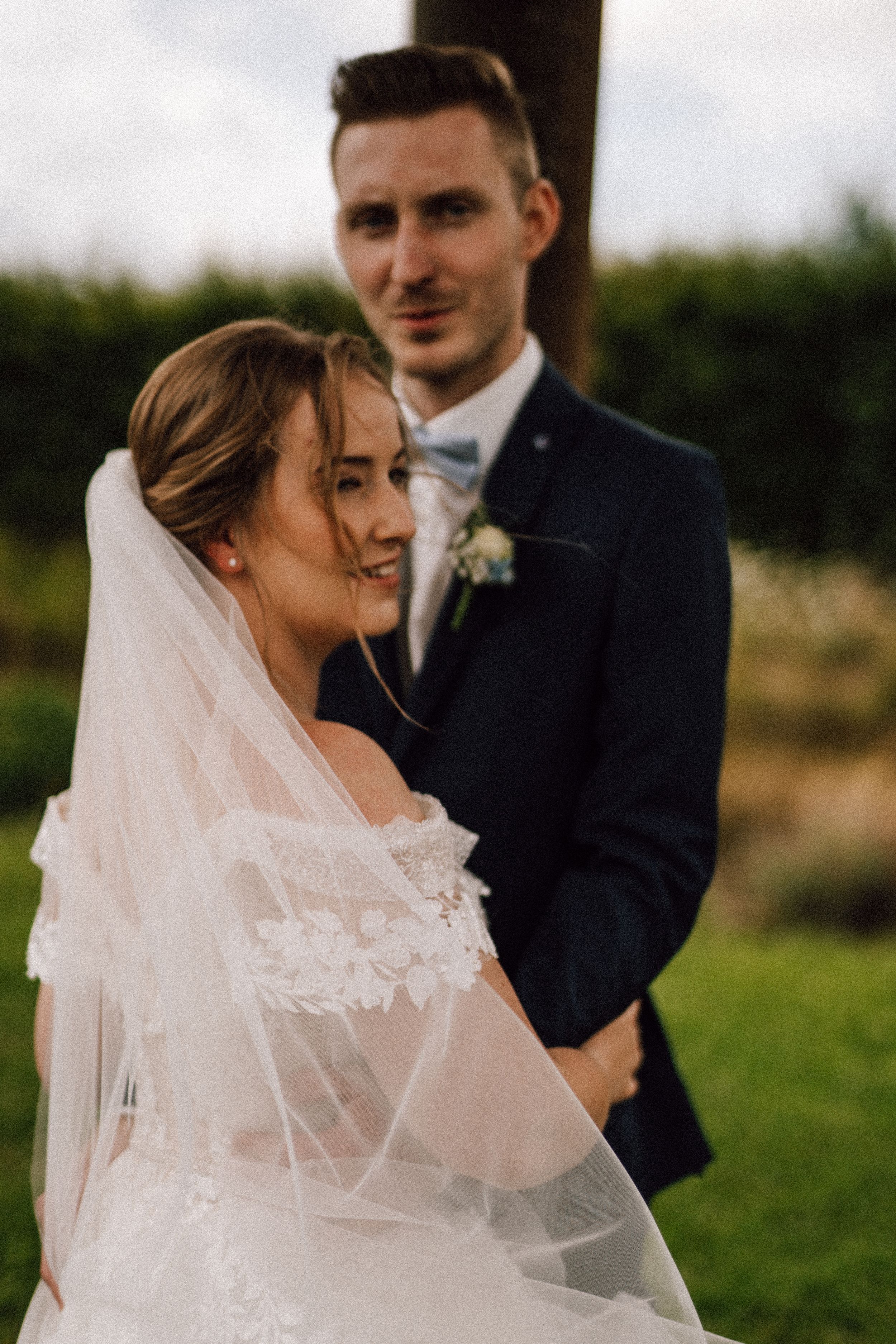 A romantic wedding portrait of a couple embracing outdoors with soft natural lighting.