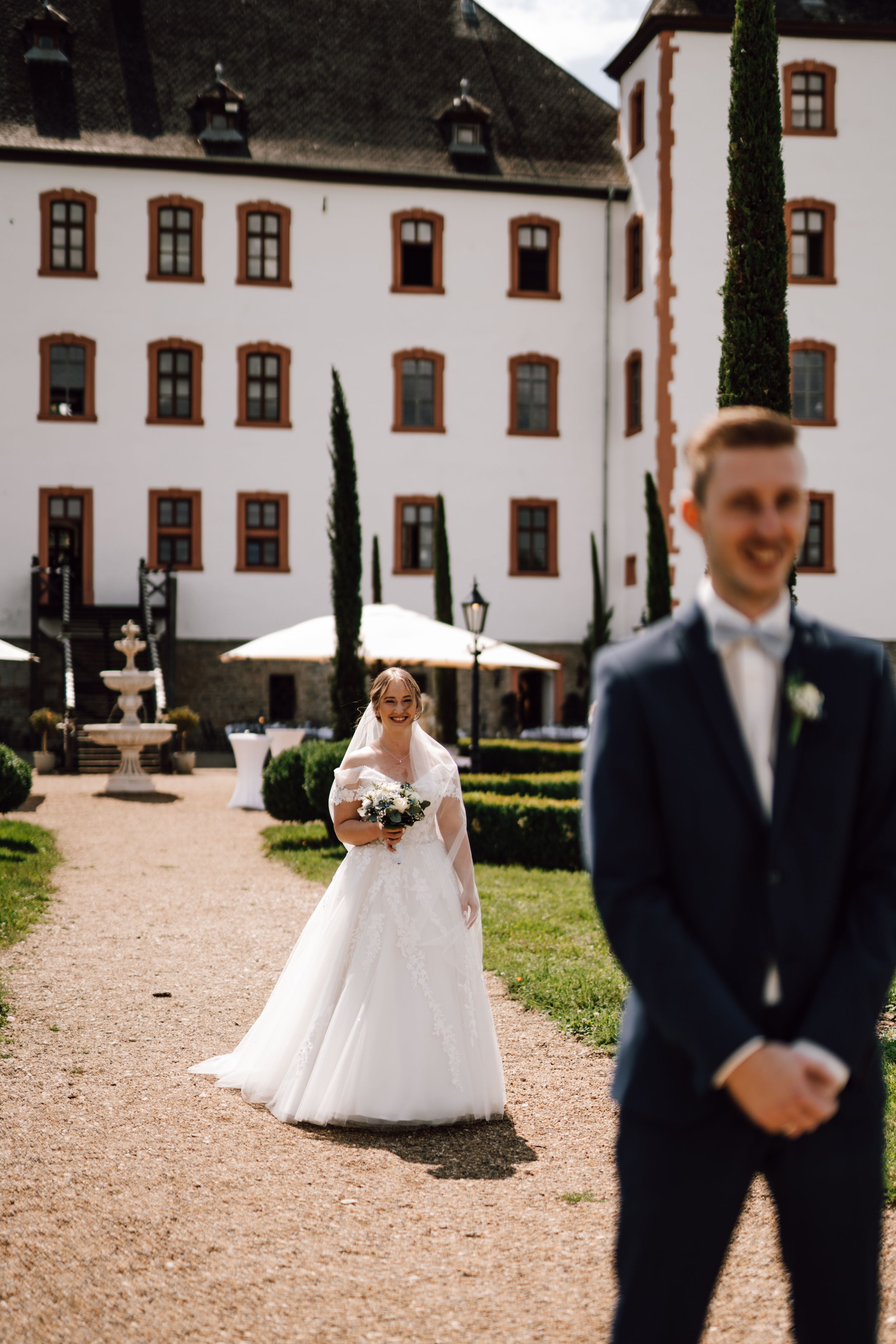 A wedding scene on a gravel path leading to a stately white building with cypress trees.