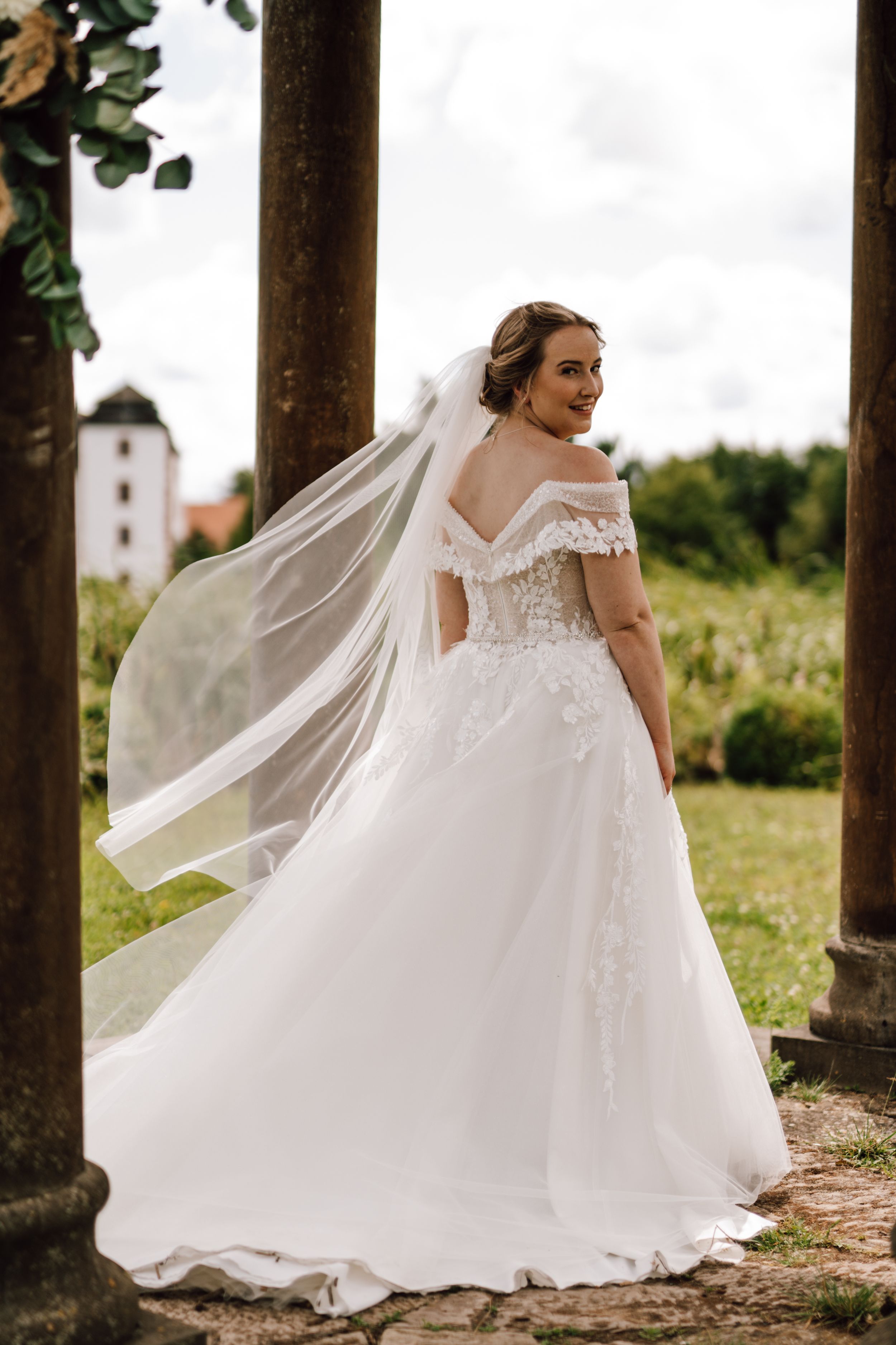 A flowing white wedding dress twirls elegantly against a backdrop of stone pillars and greenery.