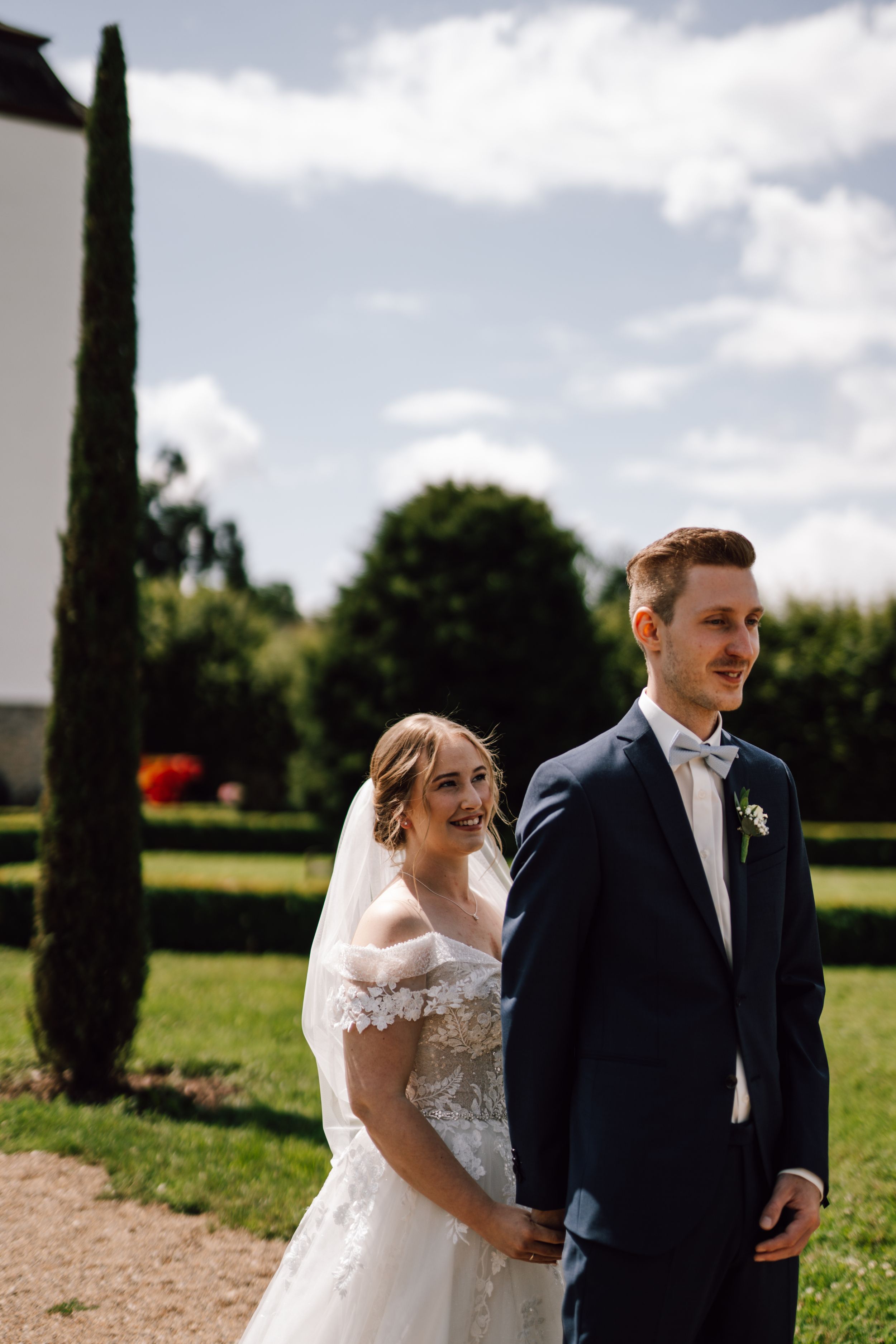 A sunny outdoor wedding scene with cypress trees and white architecture in the background.