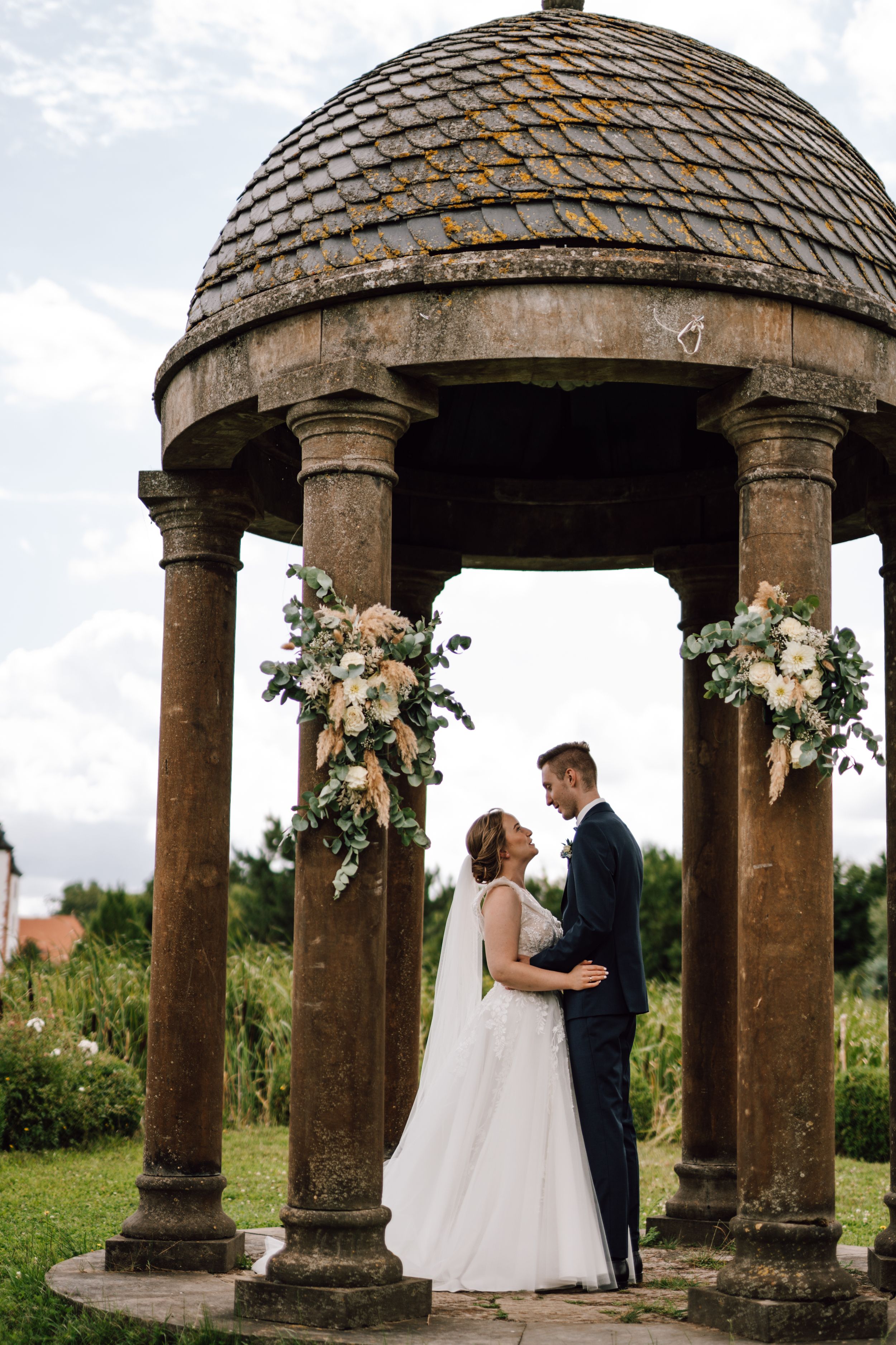 A stone gazebo decorated with floral arrangements creates a romantic wedding setting.