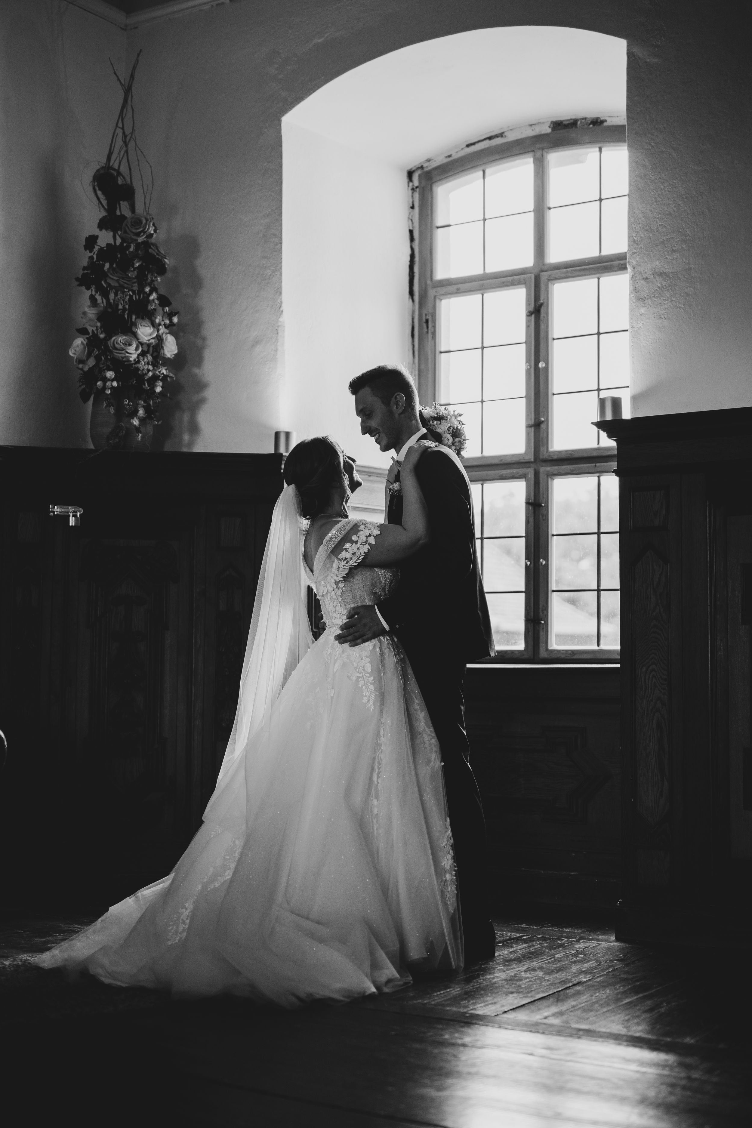 A dramatic black and white wedding portrait silhouetted against an arched window.