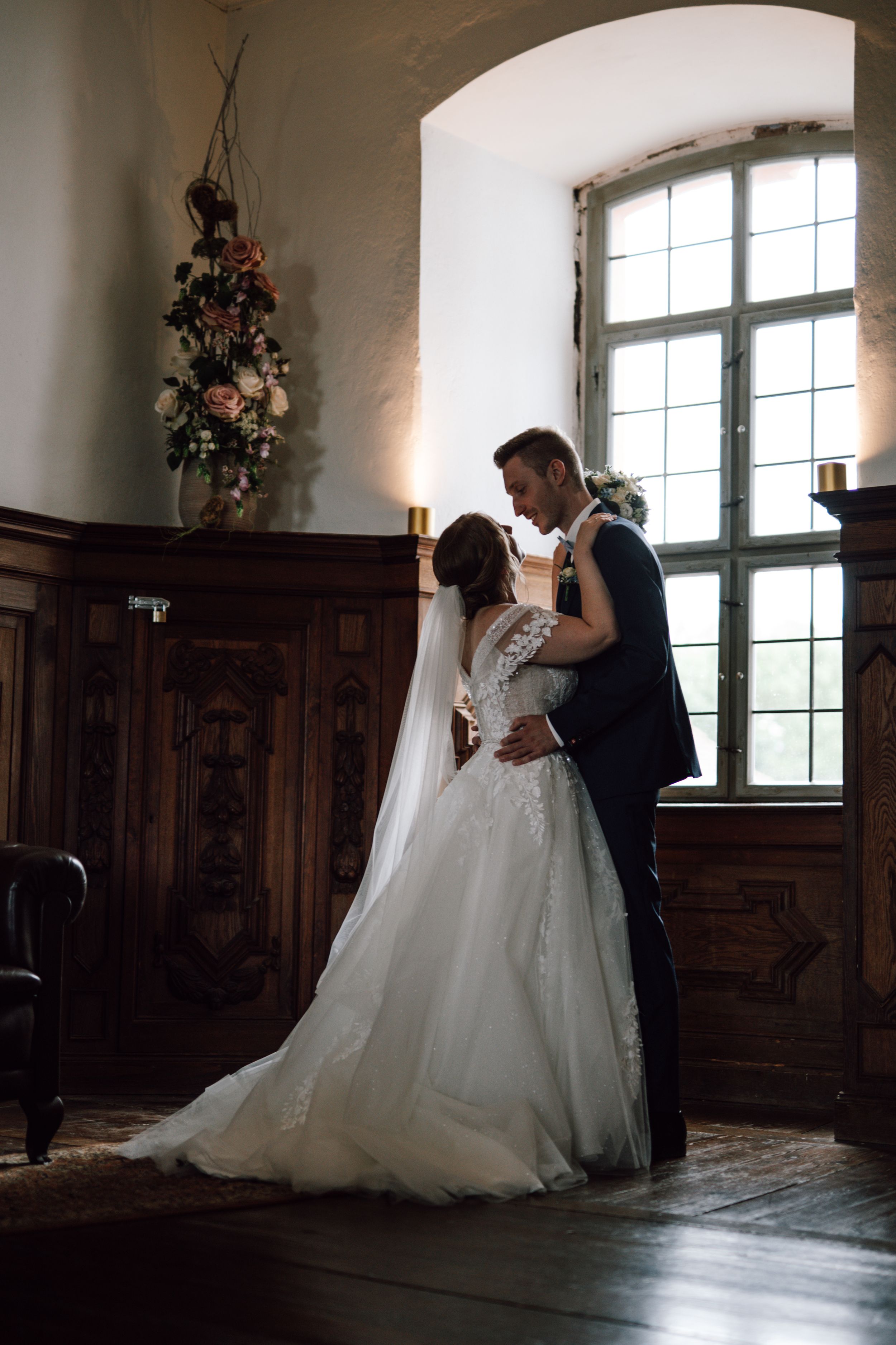 A romantic wedding moment in a historic venue with wood paneling and arched windows.