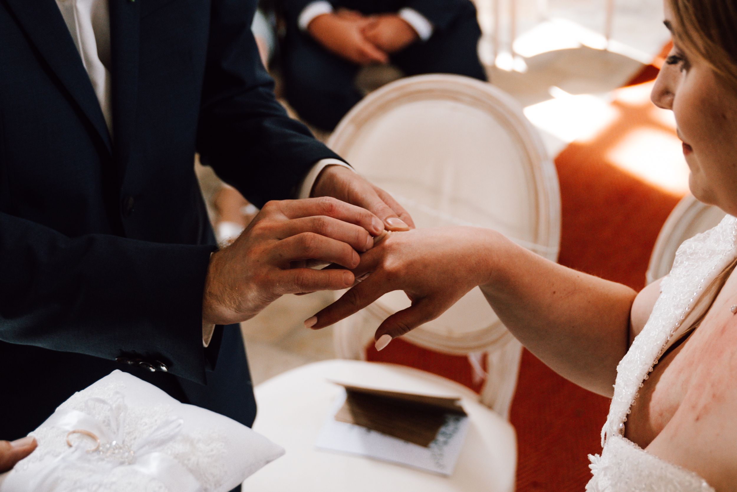 A close-up of hands exchanging wedding rings during a church ceremony.