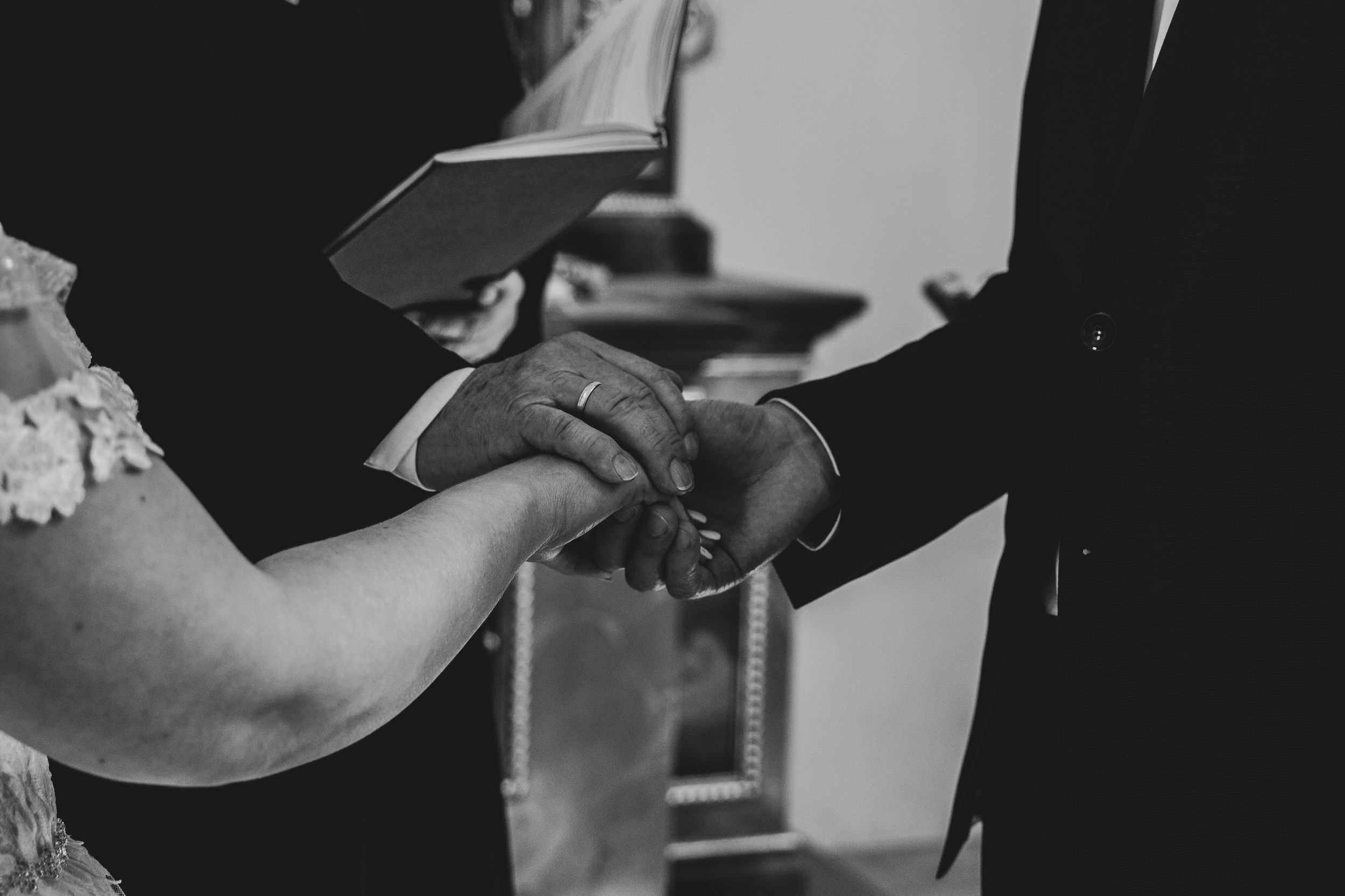 A black and white capture of hands joining during a wedding ring exchange.