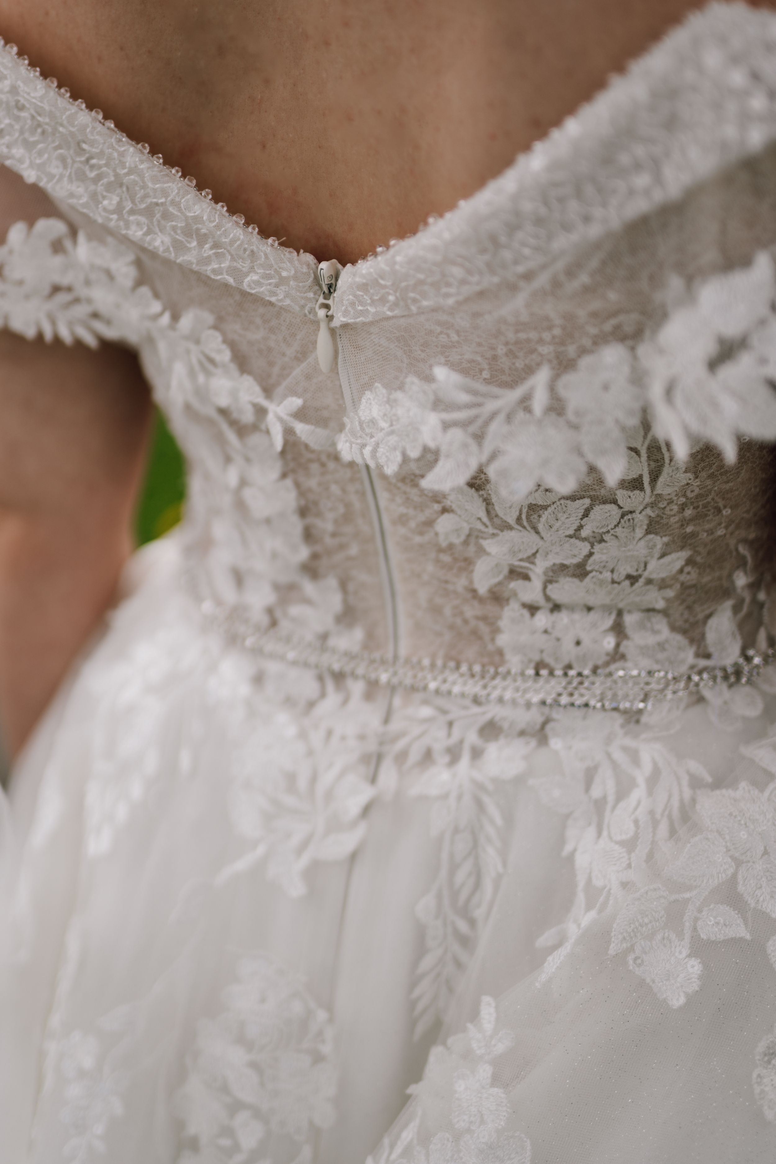 Close-up detail of delicate lace and beadwork on a white wedding dress bodice.
