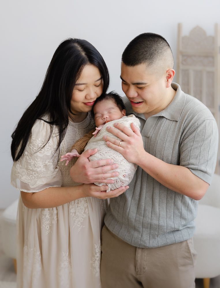 Beautiful photo of an asian couple with the newborn baby in a bright setting with beautiful natural lighting.