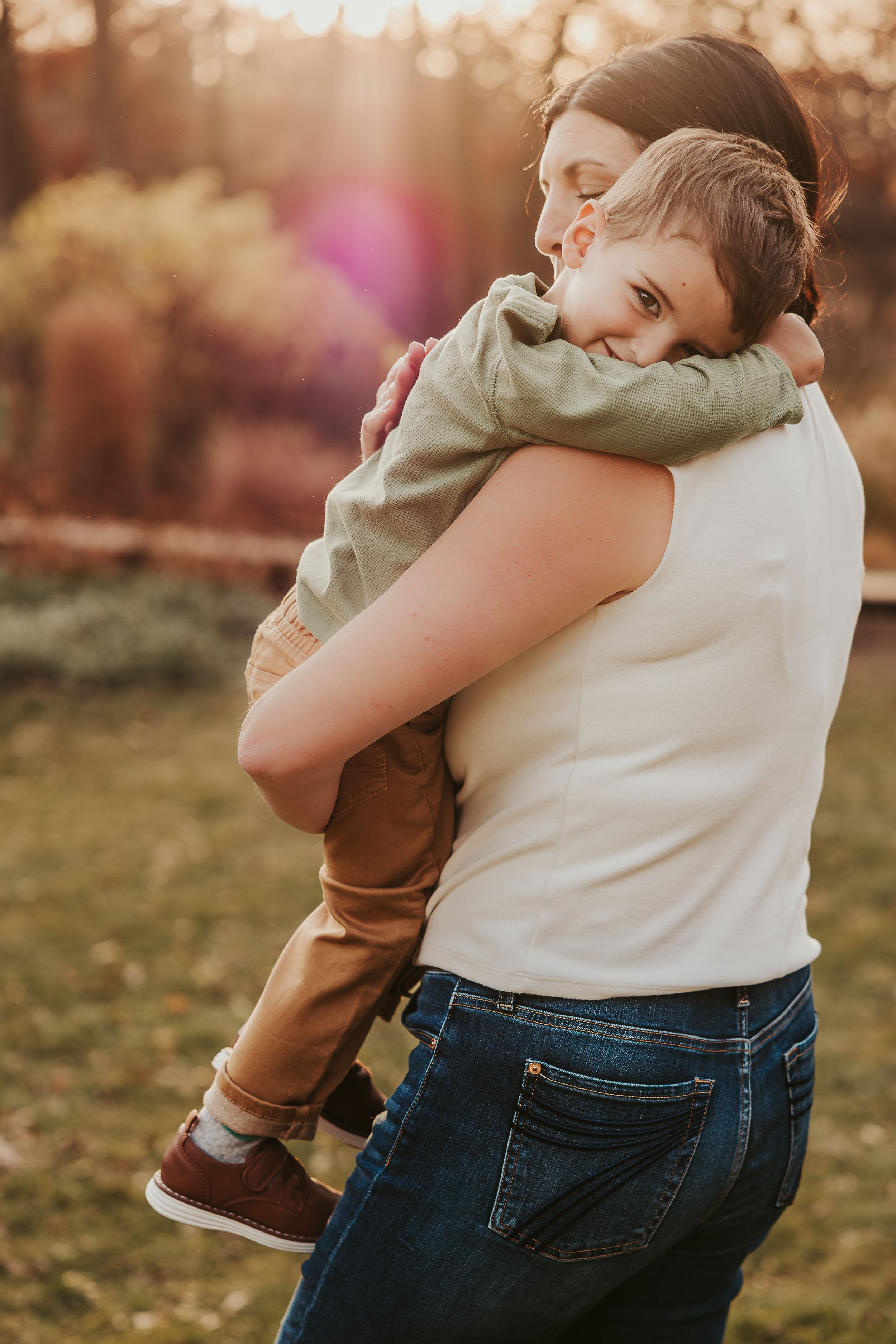 A gentle embrace between parent and child in casual clothing outdoors during golden hour.