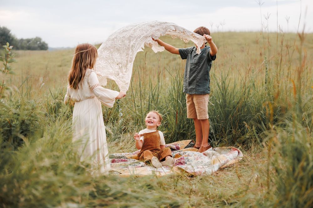 A family enjoying a picnic on a blanket in a meadow with tall grass on a summer afternoon.