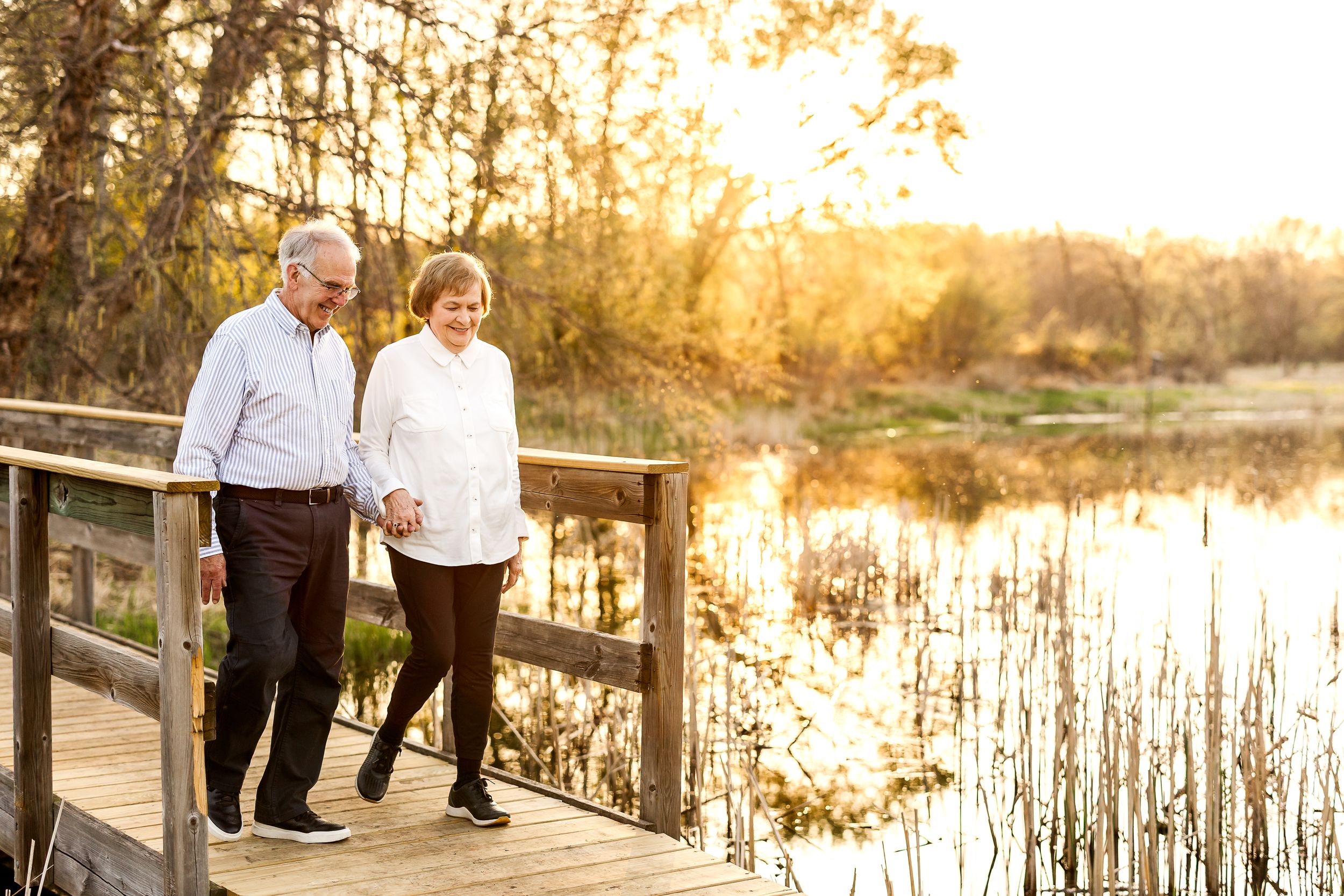 A couple walks together on a wooden boardwalk over a serene pond during golden hour sunset.