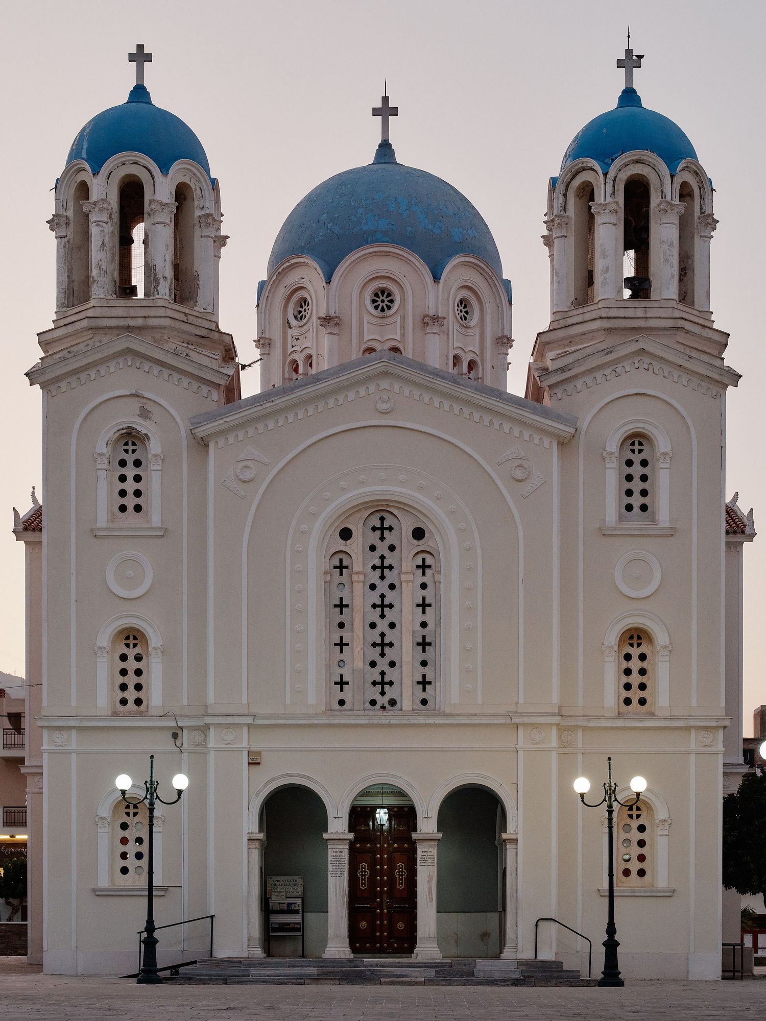 White orthodox church with blue domes and arched entrances features decorative crosses and symmetrical architecture in daylight.
