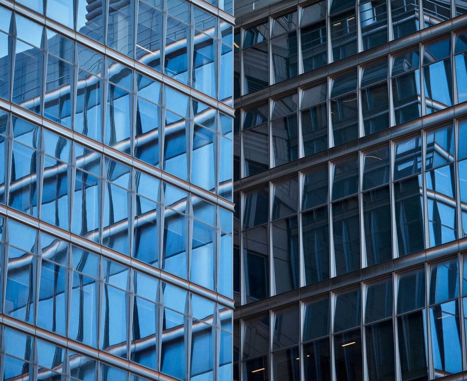 Modern glass office building exterior with geometric grid pattern reflecting blue sky.