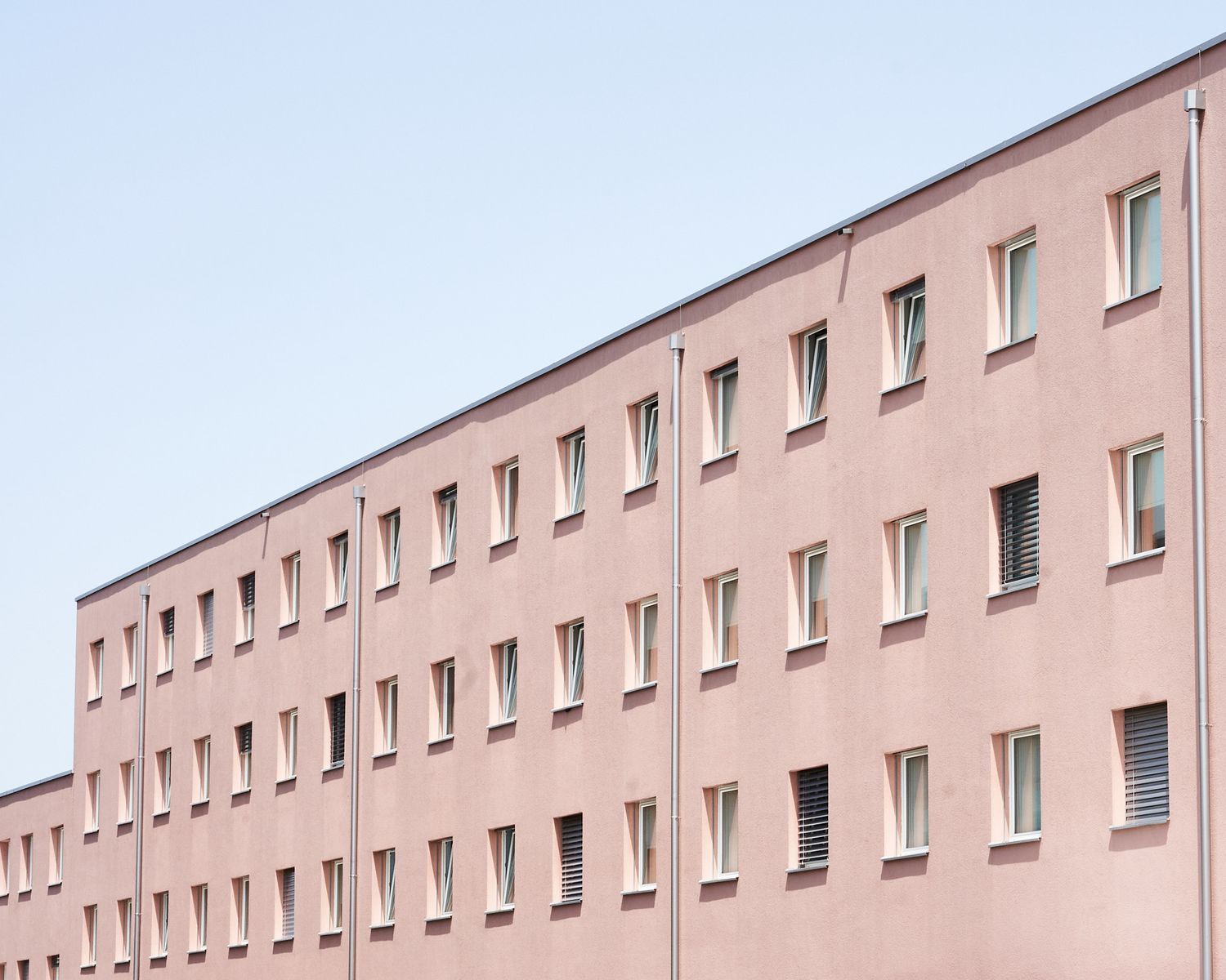 Minimalist pink apartment building facade with repetitive window pattern.