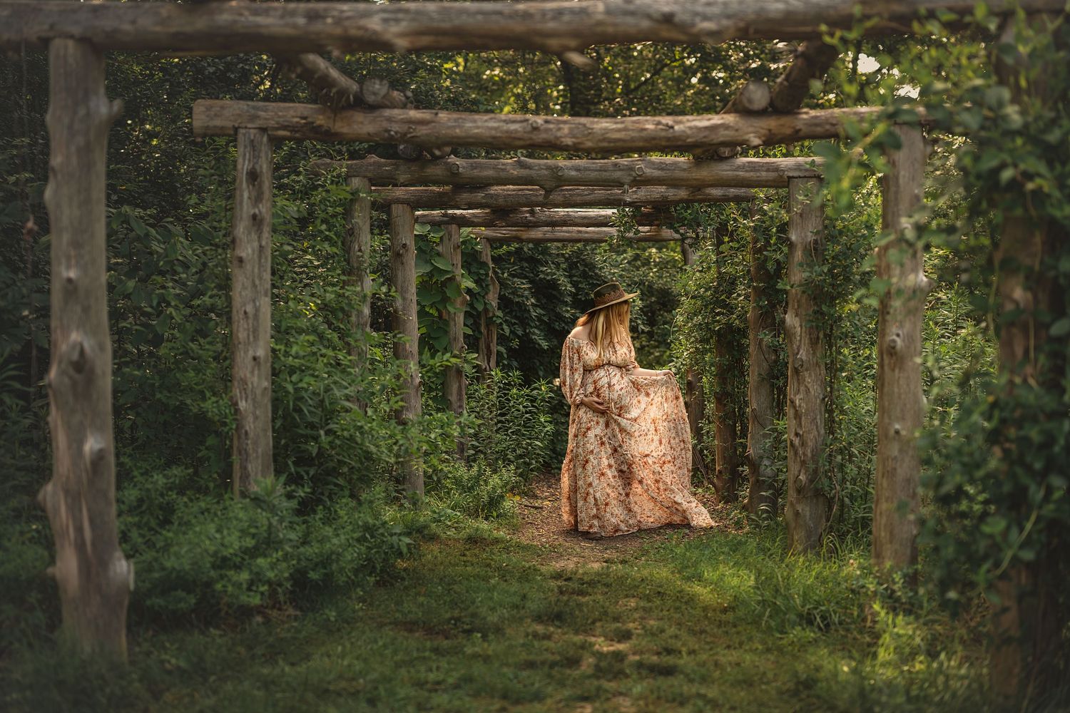 pregnant woman walks through a scenic wooden pathway of green foliage creating a natural tunnel effect in the forest for maternity photos