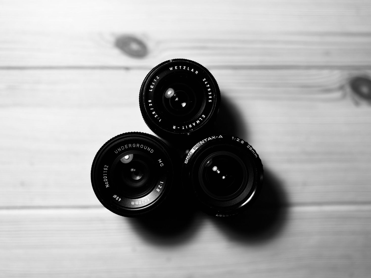 Three black camera lenses arranged in a triangle pattern on a wooden surface.