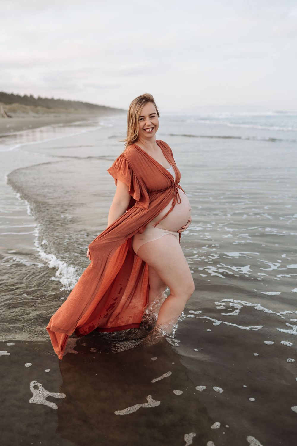 Pregnant mother wearing a rust dress on beach