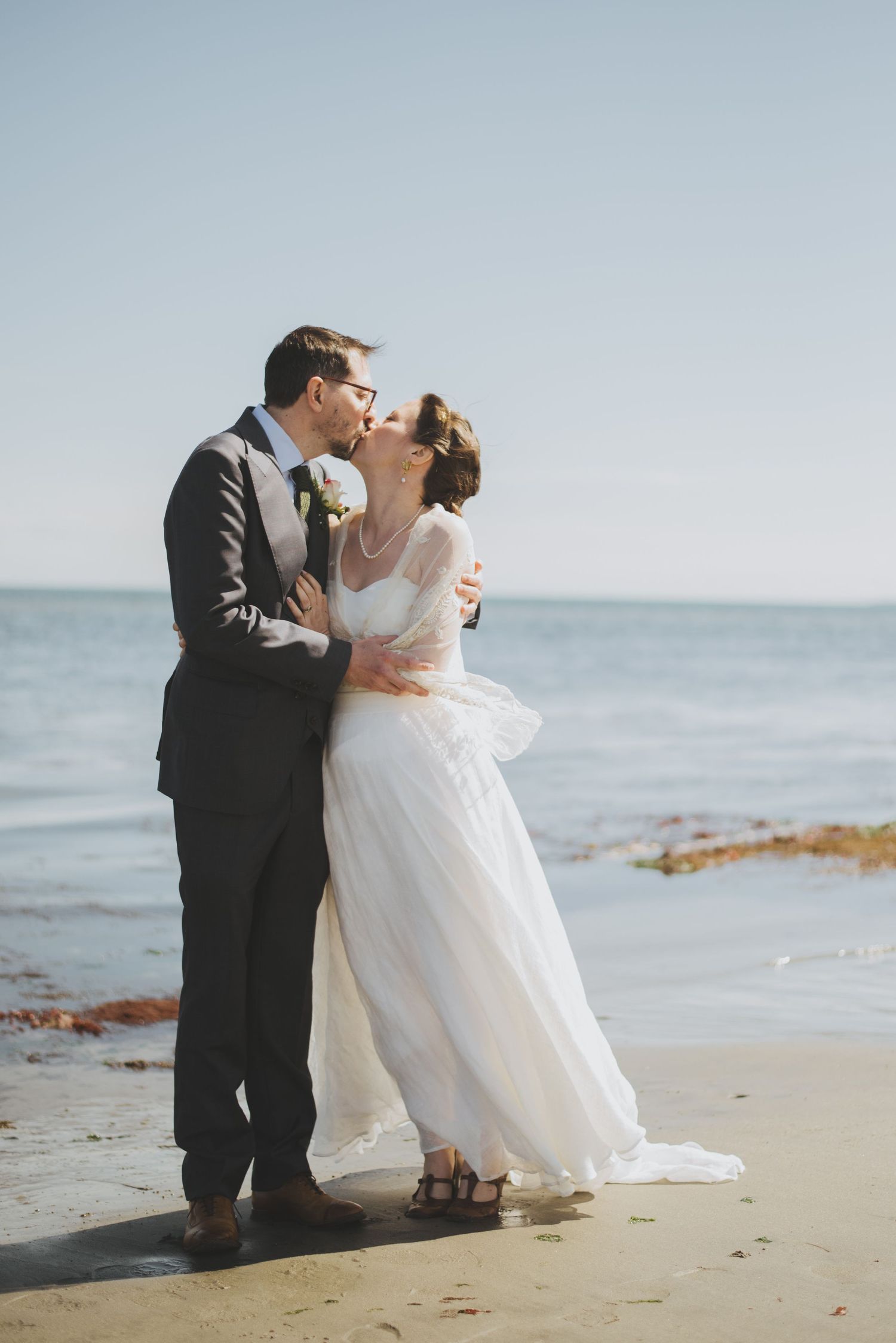 A romantic moment shared between newlyweds on a beach with ocean waves in the background.