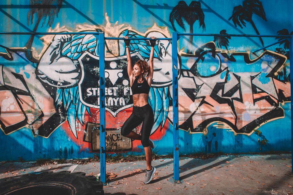 Urban dancer poses against vibrant graffiti wall with palm tree shadows.