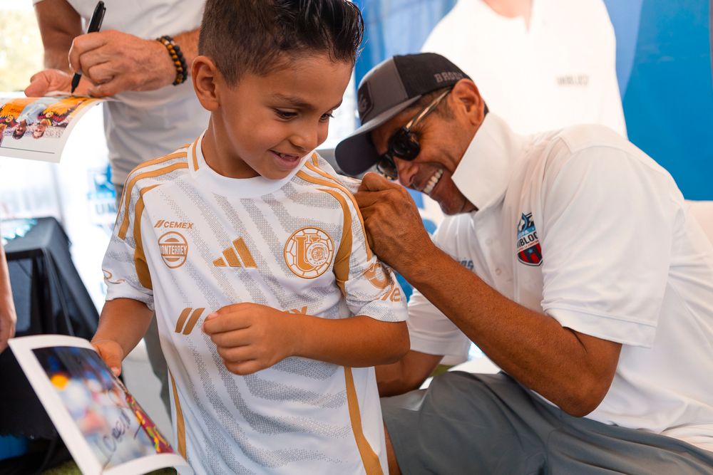 People in white shirts signing autographs for fans at an outdoor event.