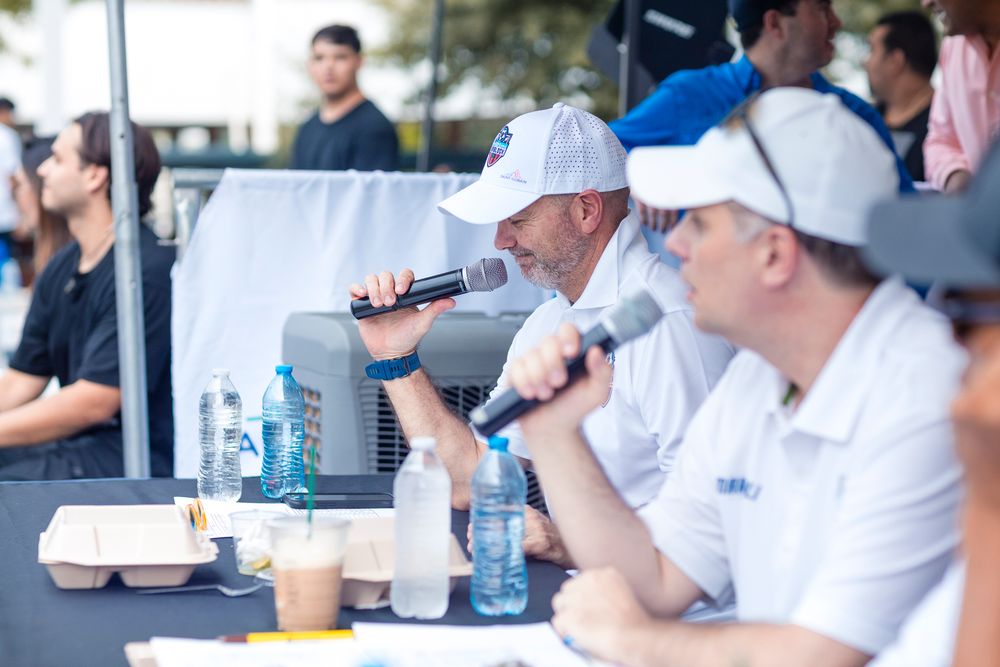 People in white shirts sit at tables during what appears to be a business meeting or seminar event.