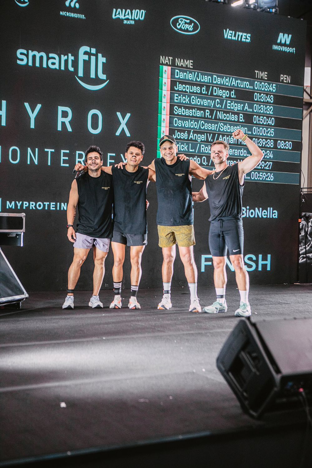 Four athletes celebrate on stage at HYROX Monterrey fitness competition, sponsored by Smart Fit and MyProtein.