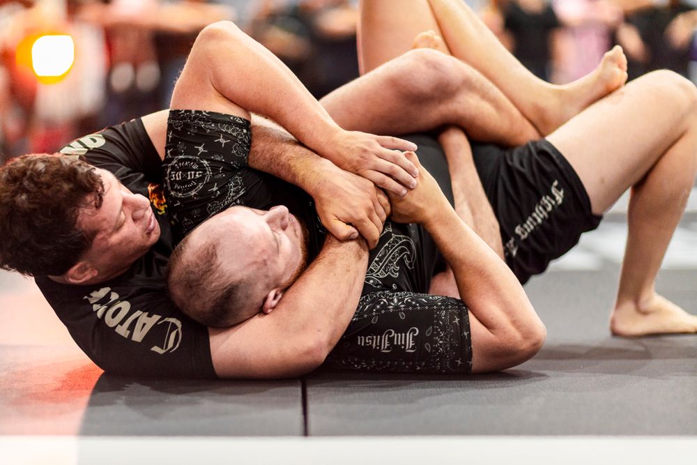 Two athletes grappling on a mat during an intense mixed martial arts match.