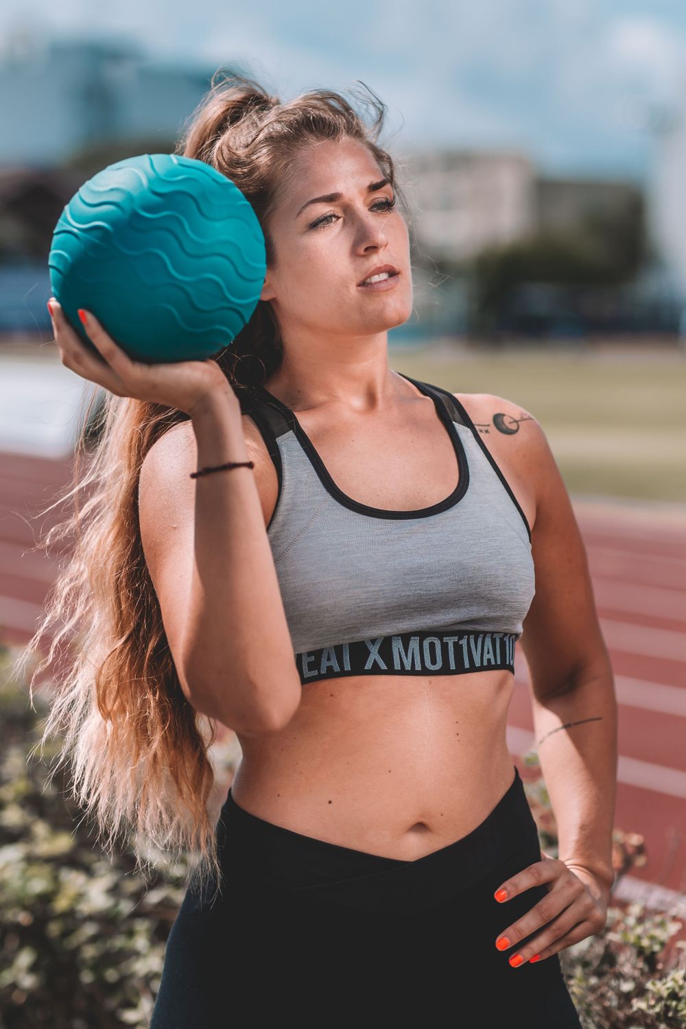 Athletic woman in sportswear holding a teal medicine ball during outdoor training session.