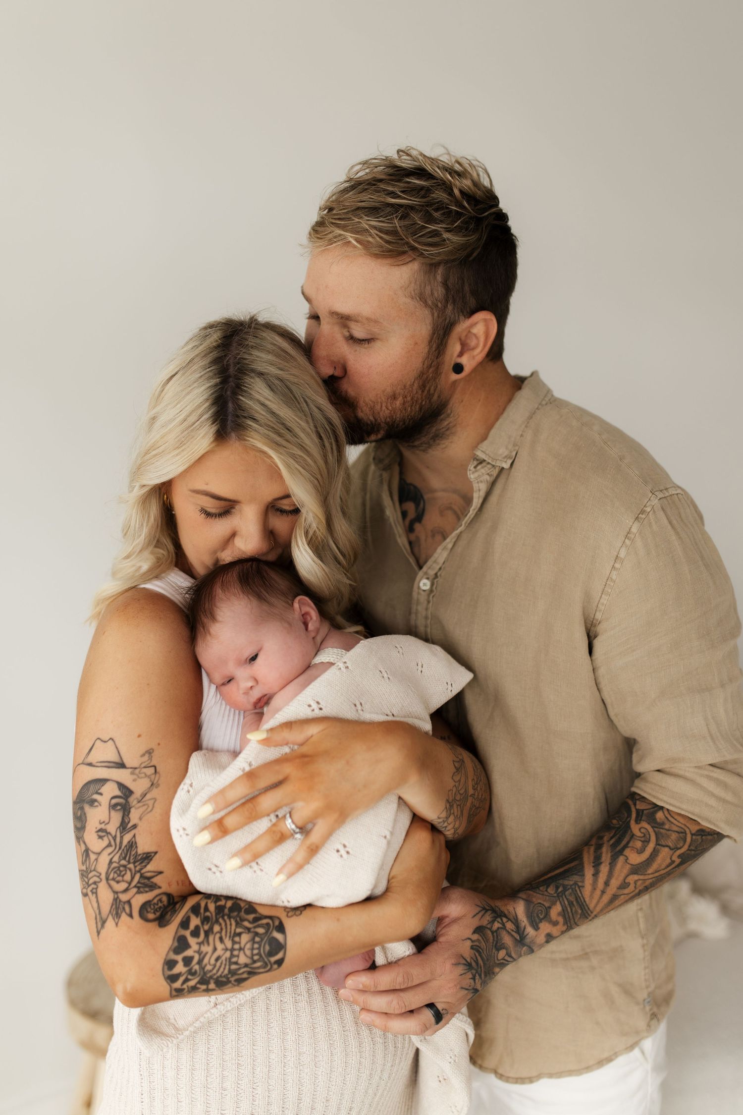 Intimate family portrait with new baby in white against neutral background.