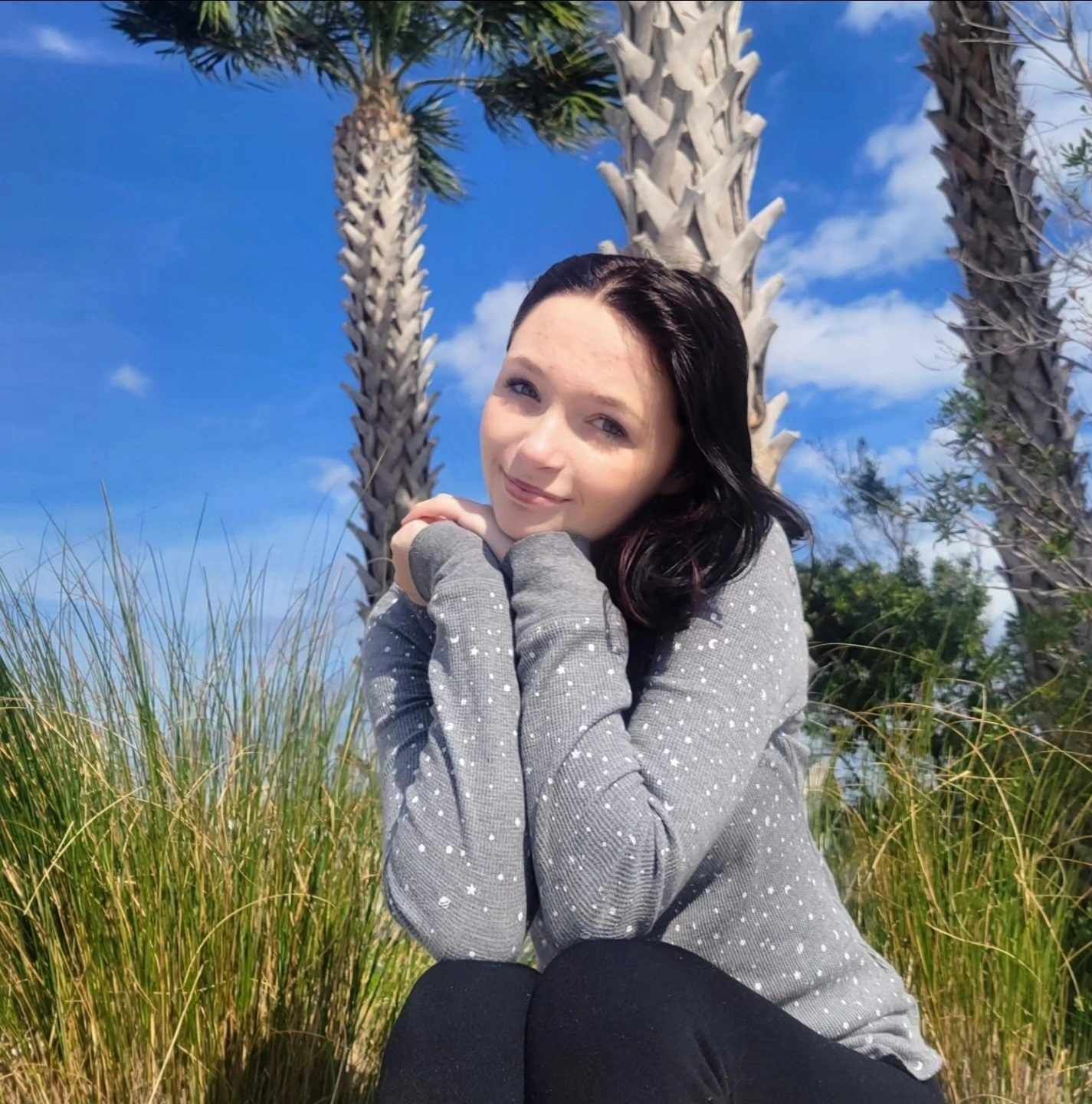 Outdoor portrait at beach with palm trees against bright blue sky.
