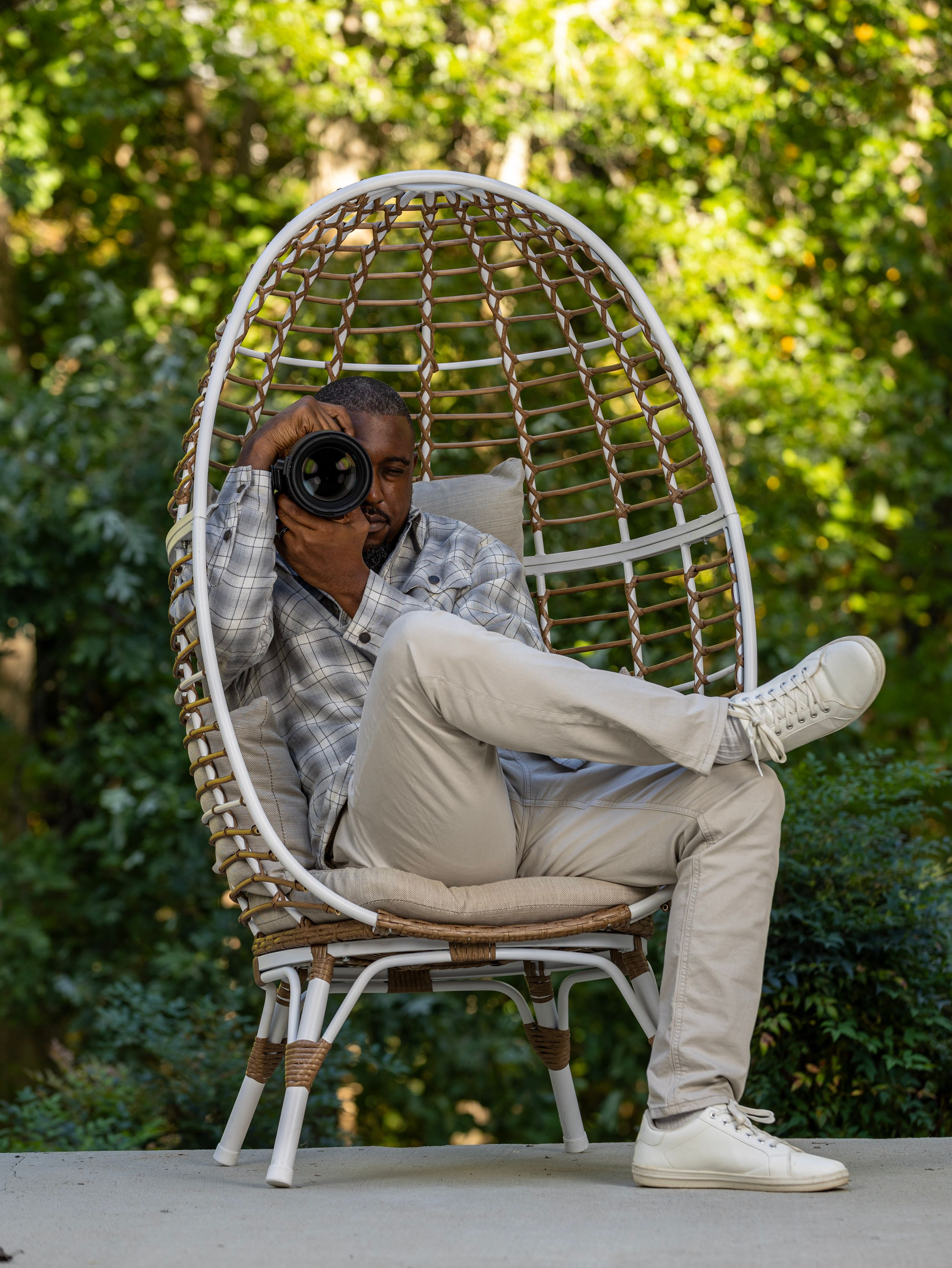Person in casual attire taking photos while lounging in modern white outdoor chair. | Shot By Lo™