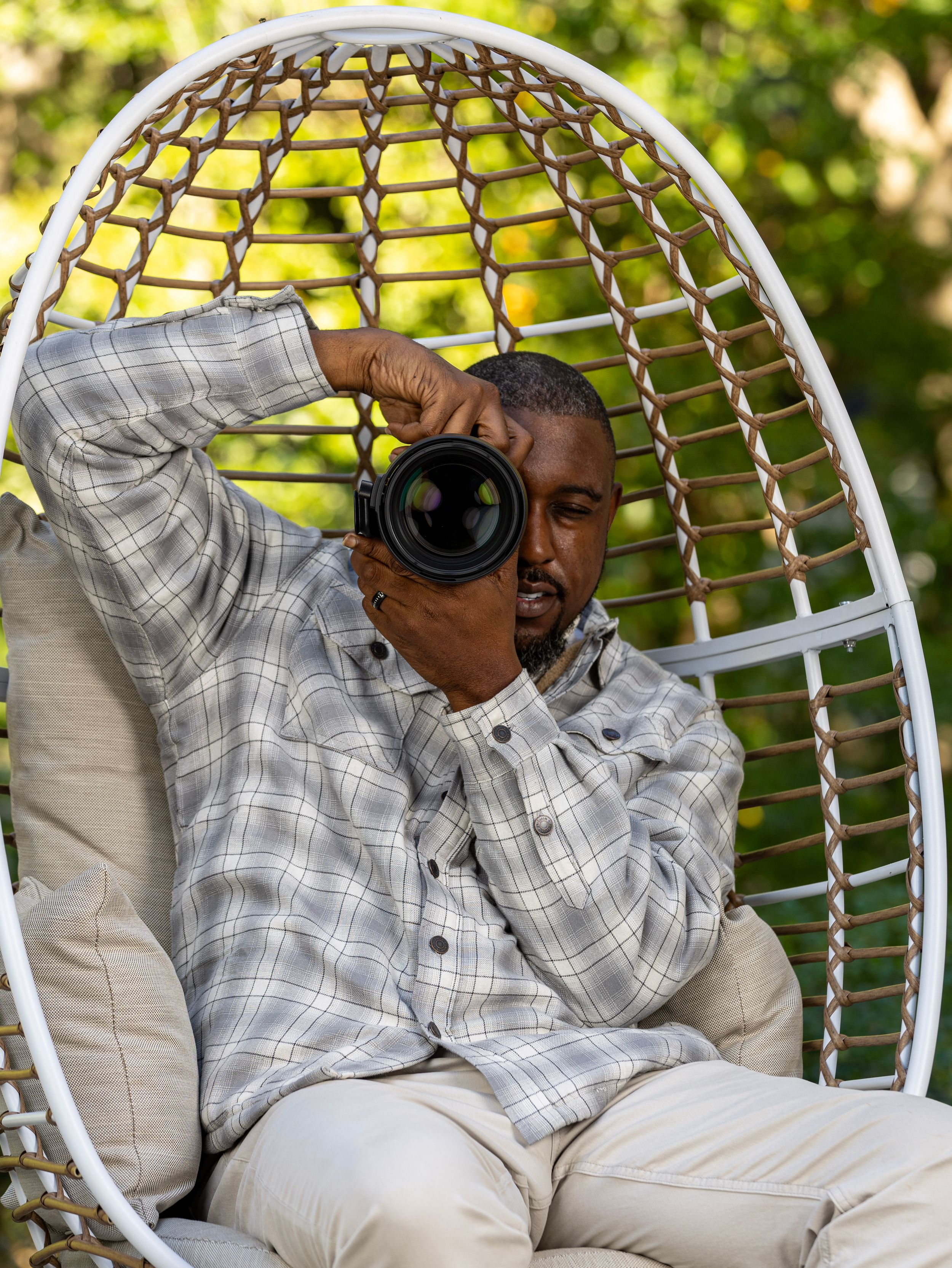 Photographer in plaid shirt taking pictures while seated in white outdoor egg chair. | Shot By Lo™