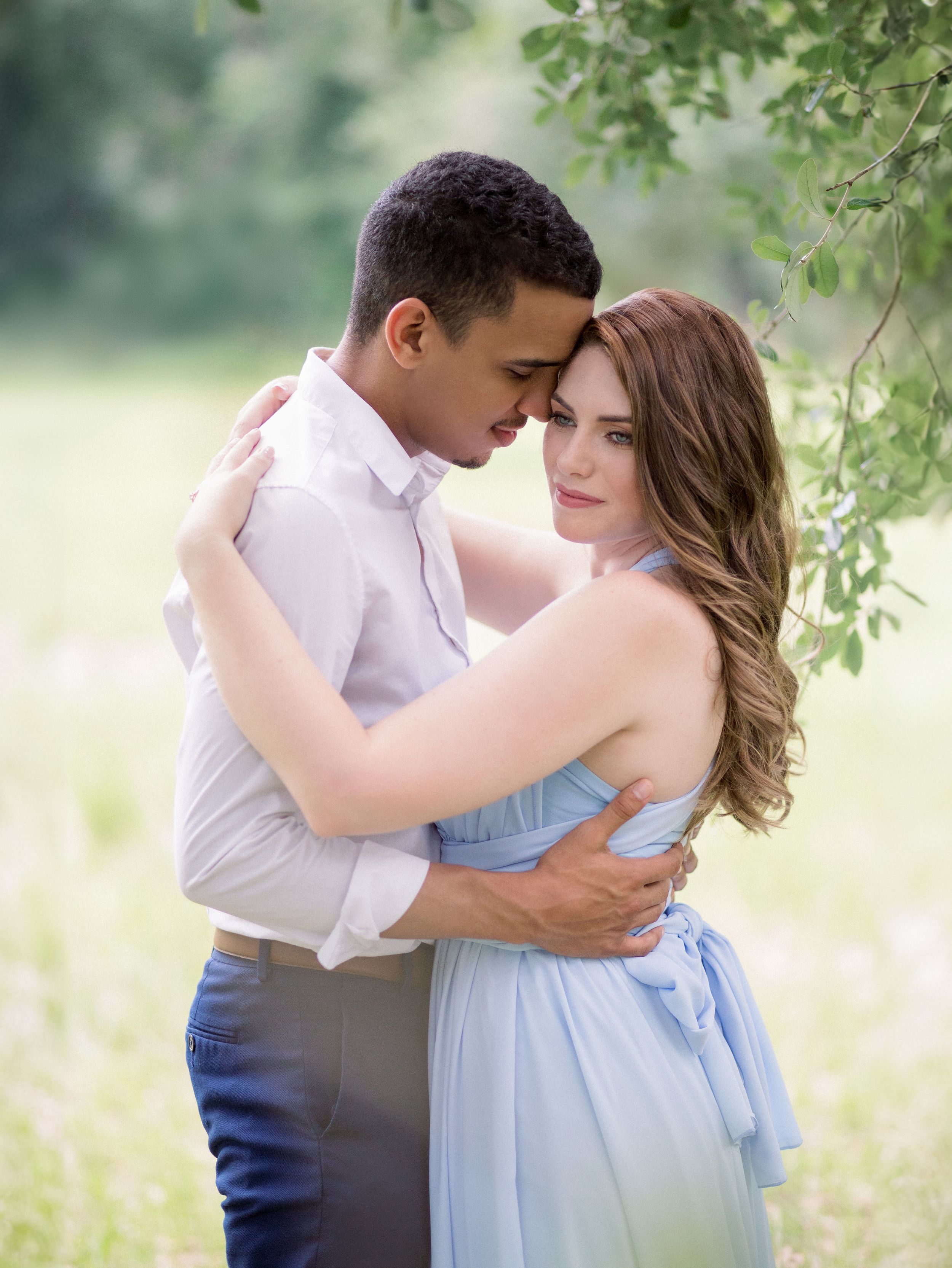 A romantic embrace between couple in pastel attire under tree branches.