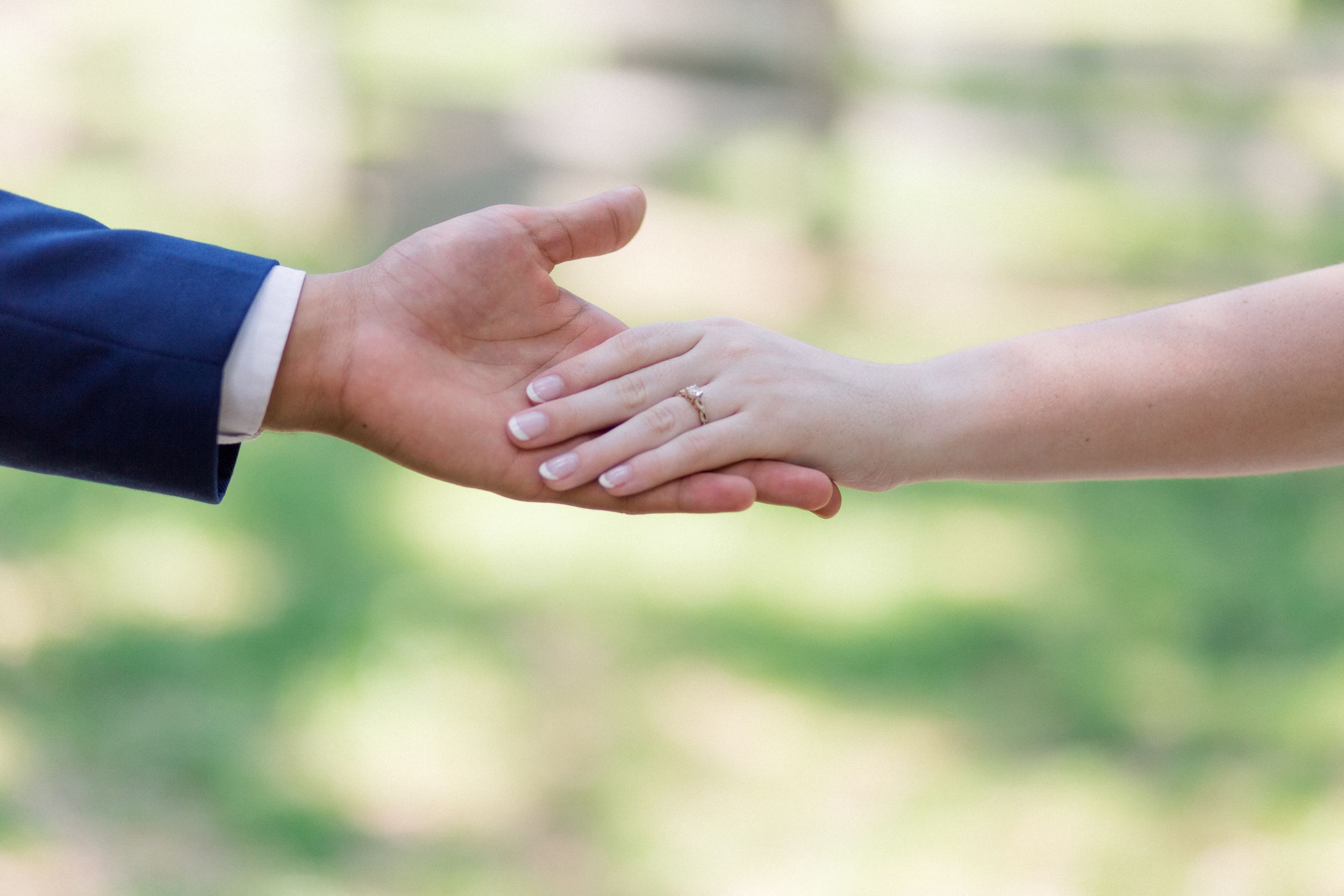 Two hands reaching toward each other against a blurred nature background in a romantic gesture.