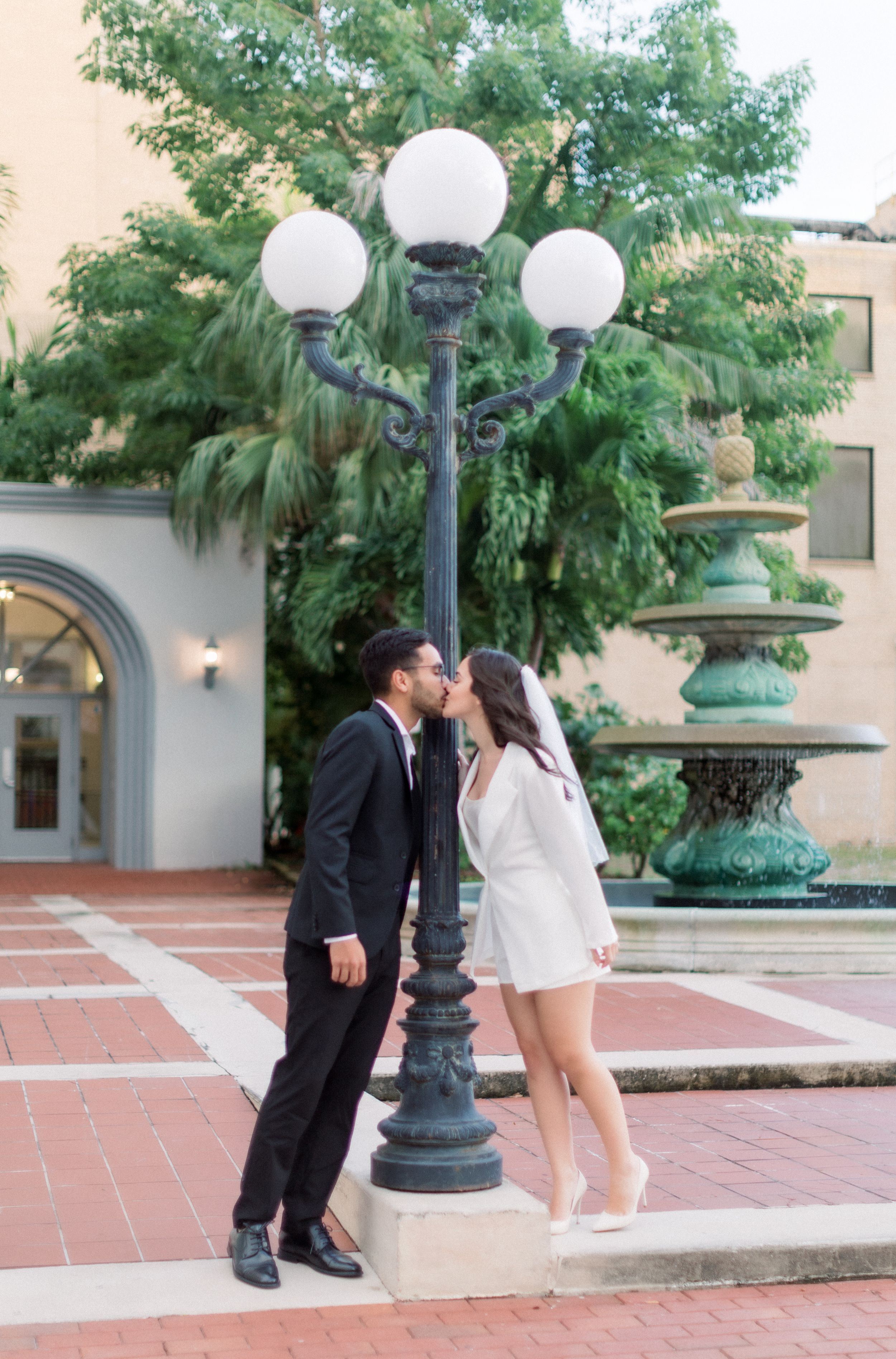 A couple embraces beneath vintage street lamp on brick courtyard.