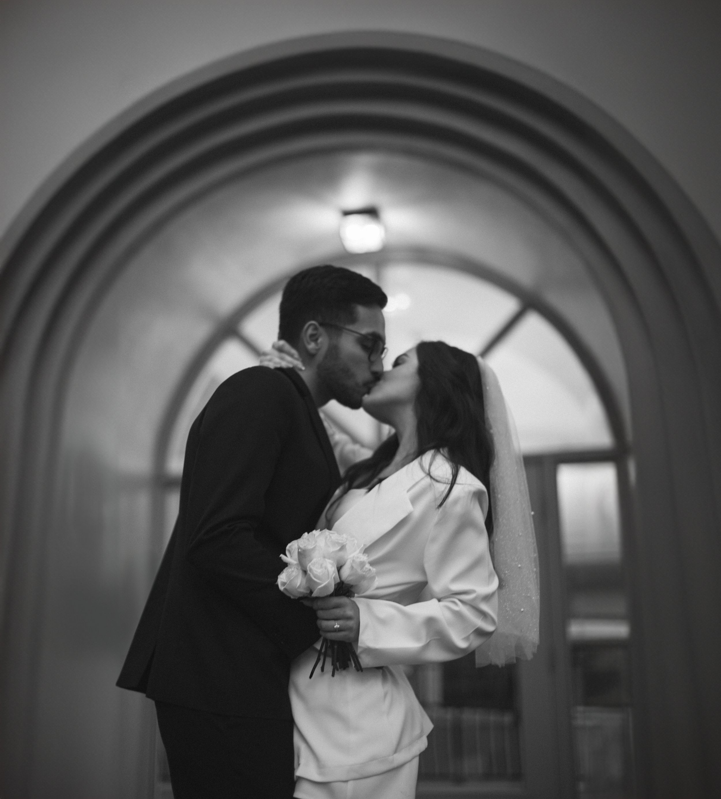 A romantic black and white photo of a couple kissing under an arched doorway.