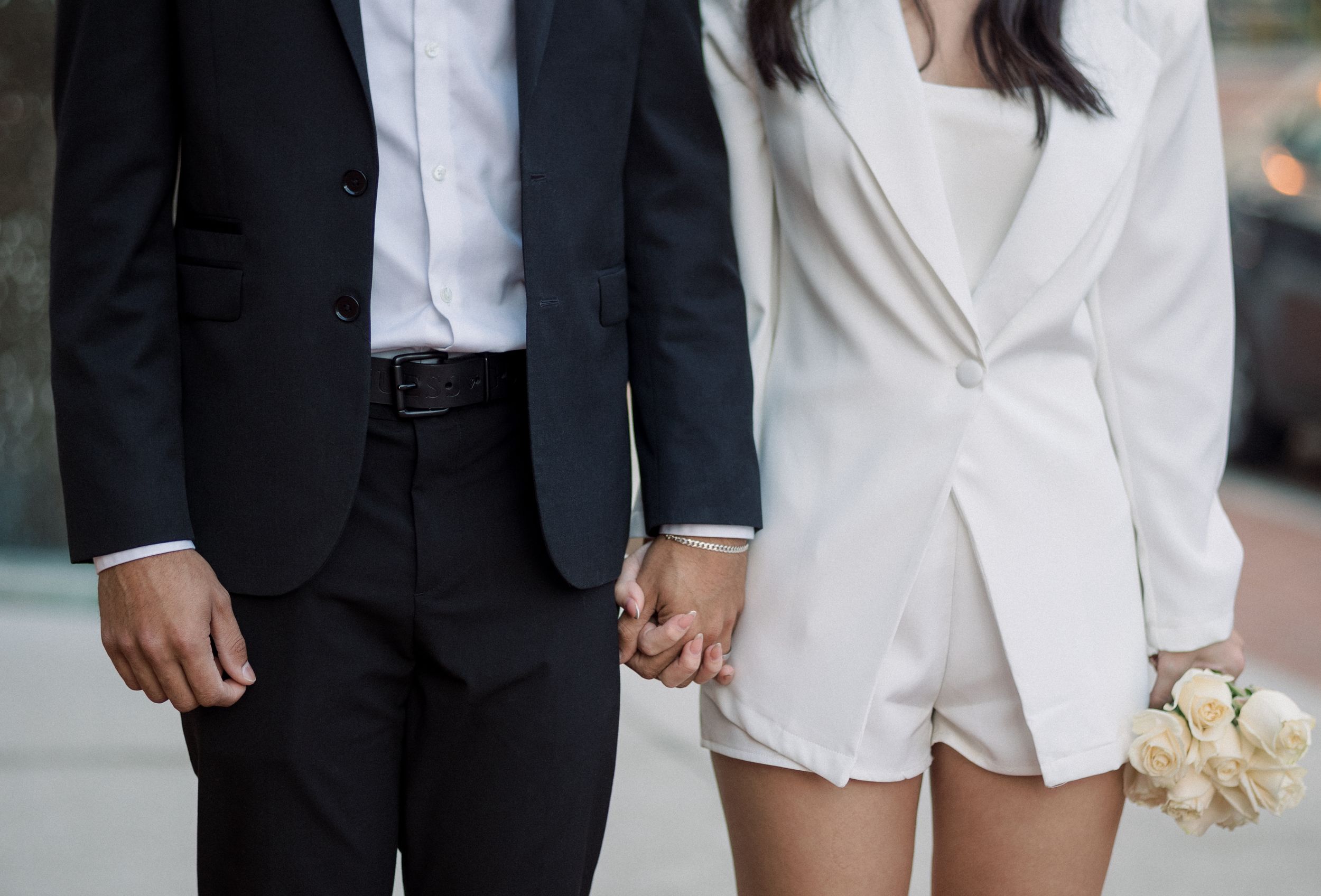A couple in formal attire holding hands with white roses.