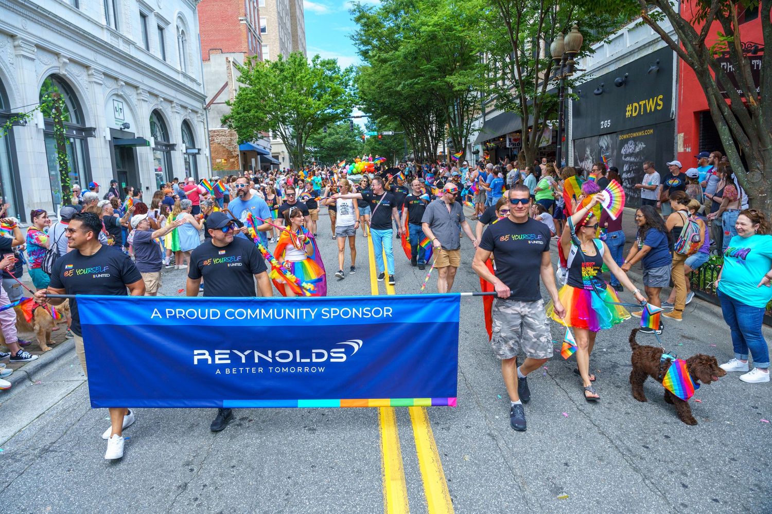 Large crowd marching in Pride parade with Piedmont banner on urban street.