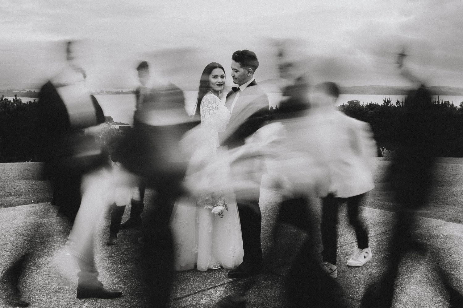 Blurred motion of people dancing in formal attire at an outdoor wedding reception in black and white.