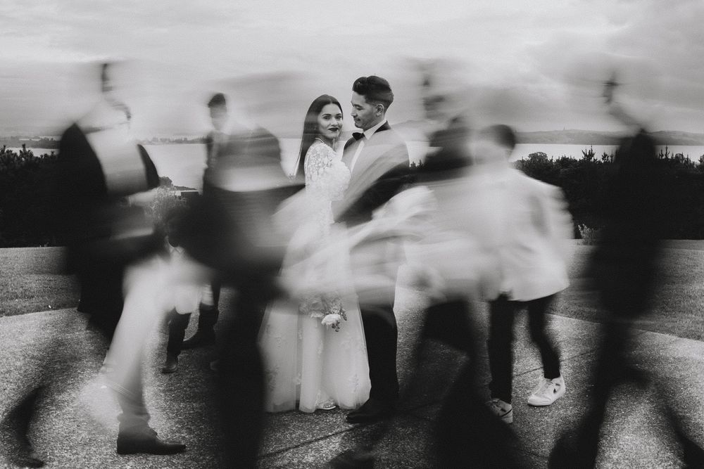 Blurred motion of people dancing in formal attire at an outdoor wedding reception in black and white.