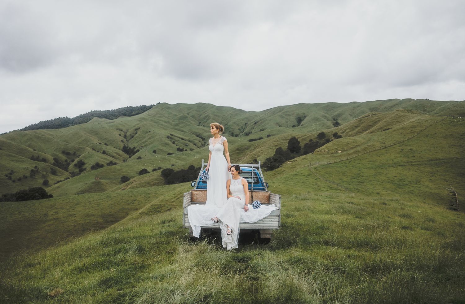 LGBTQ+ Same-sex wedding: brides riding in the back of a truck while exploring their farm. Auckland photographer.