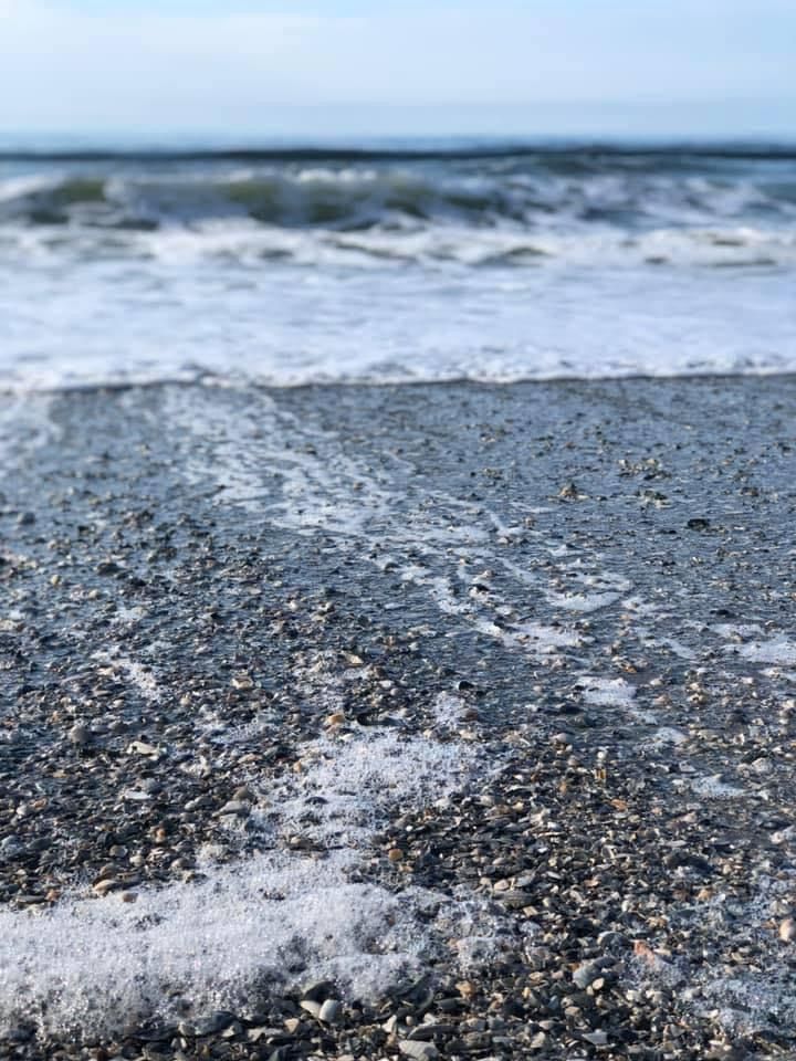 Close-up of ocean waves washing over a pebbly beach with sea foam.