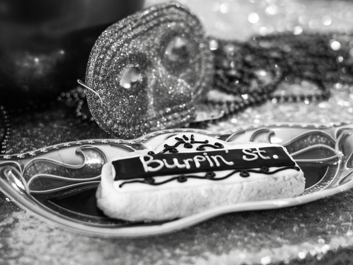 Black and white photo of birthday cookies with decorative silver mask on glittery surface.
